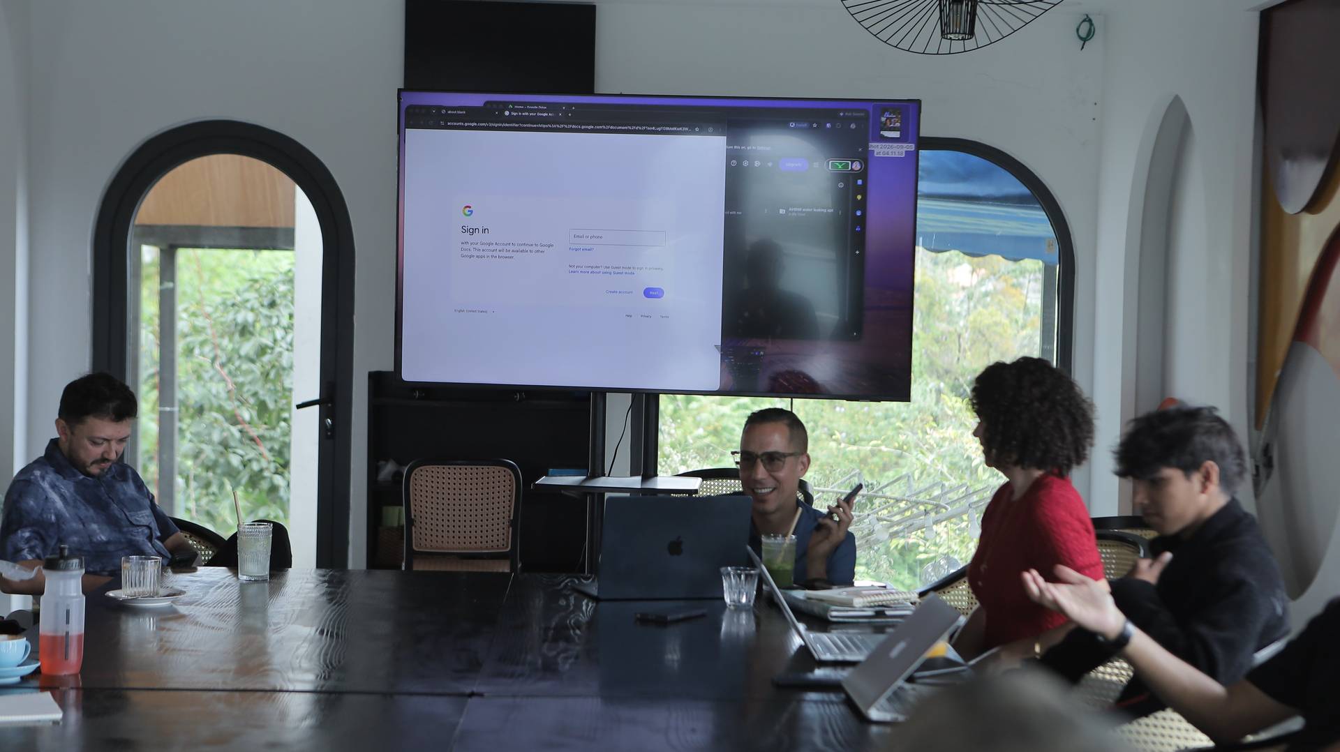 A group of people engaged in a collaborative meeting or presentation in a modern Vietnamese setting with large windows and lush greenery visible outside.