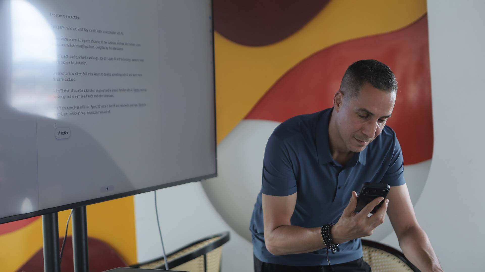 A man is engaged with his phone in a vibrant setting during a workshop roundtable discussion about AI in Đà Lạt, Vietnam.