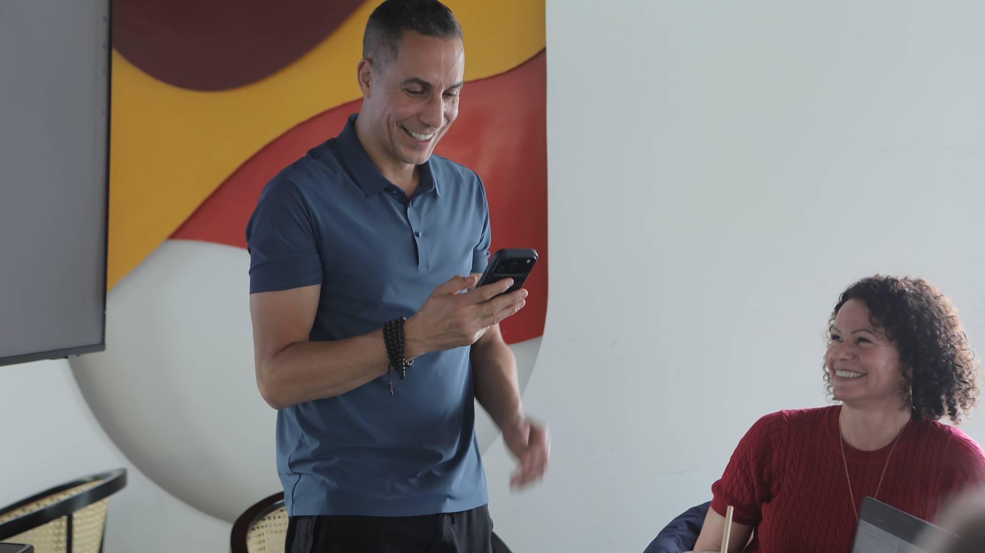 A man in a blue polo shirt smiles while holding his phone during what appears to be a casual gathering or presentation in Đà Lạt, Vietnam.