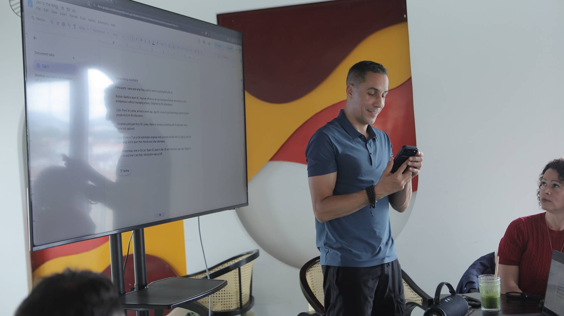 A man stands in front of a large screen displaying notes from a workshop roundtable discussion about AI in Đà Lạt, Vietnam.