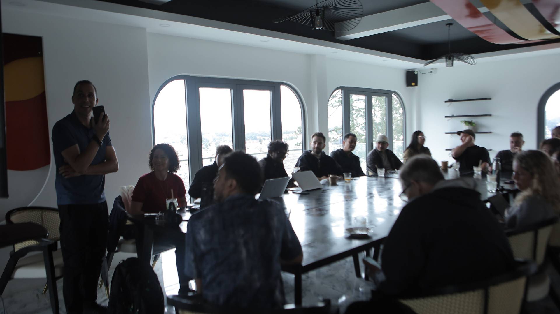 A group of people gathered around a long table in a modern, well-lit room with large windows overlooking Đà Lạt's scenic landscape, engaging in what appears to be a collaborative meeting or brainstorming session.