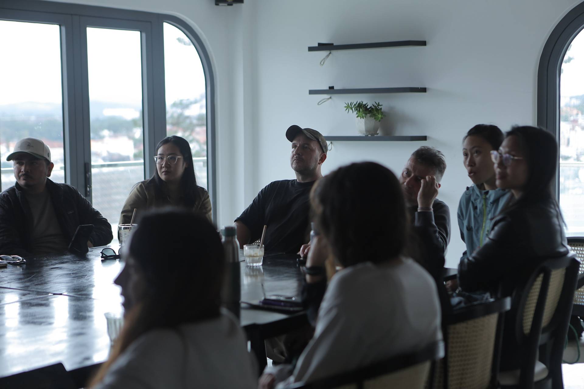 A group of individuals engaged in a discussion around a table with a scenic view of Đà Lạt's landscape in the background.