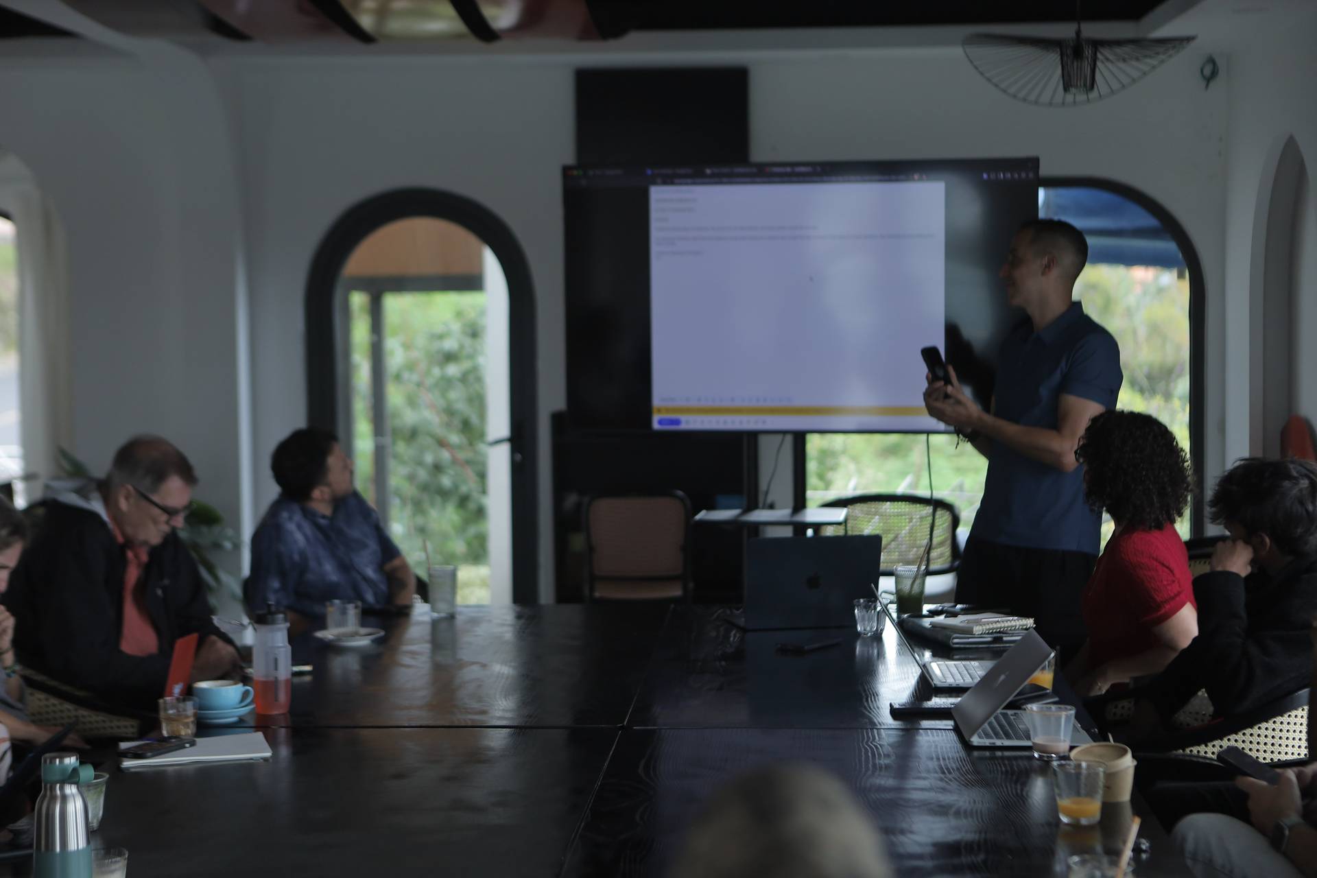 A professional meeting in a modern conference room with attendees focused on a presentation displayed on a large screen.