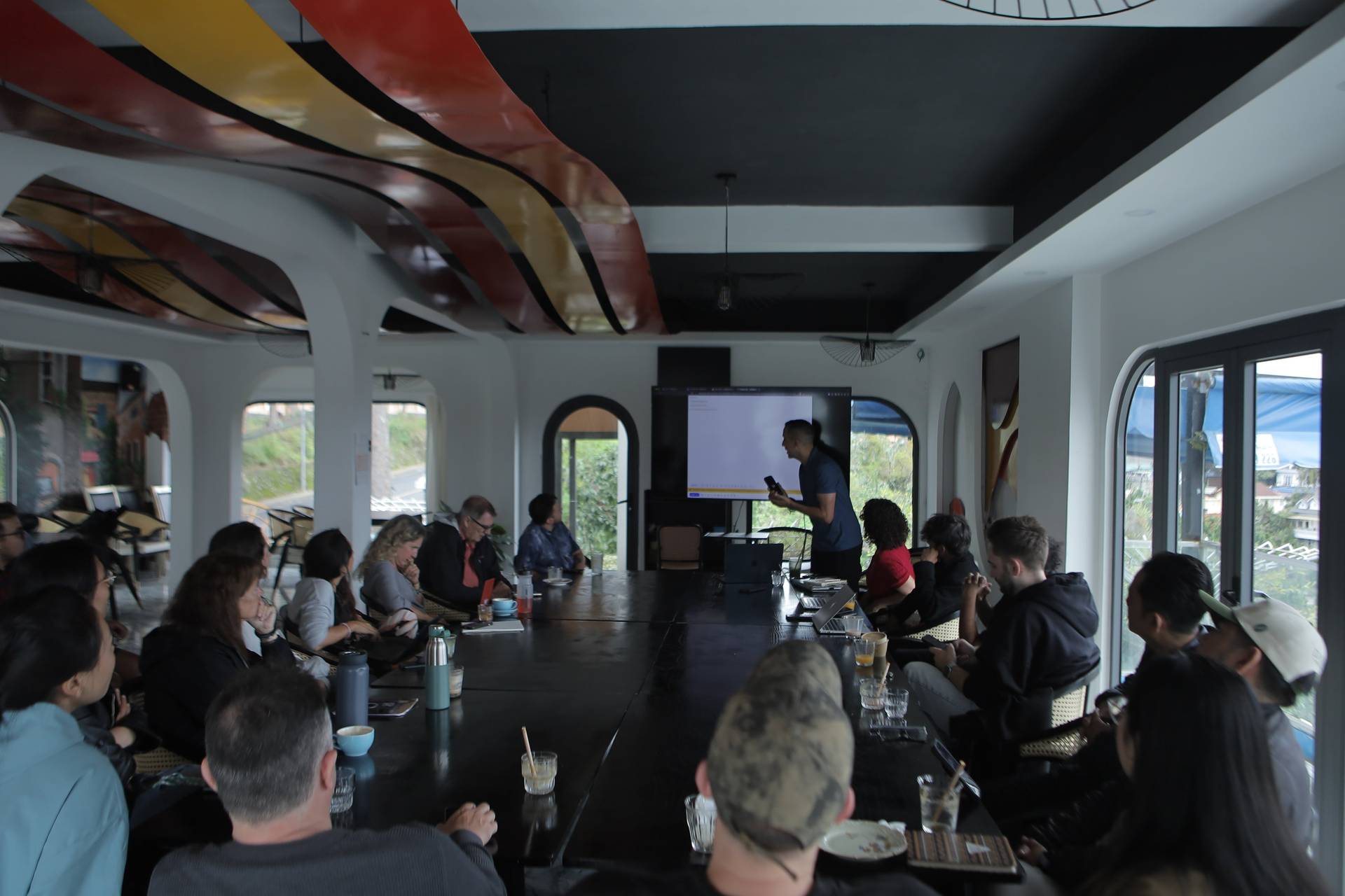 A group of people is gathered in a modern conference room in Đà Lạt, Vietnam, attentively listening to a presentation projected onto a screen.