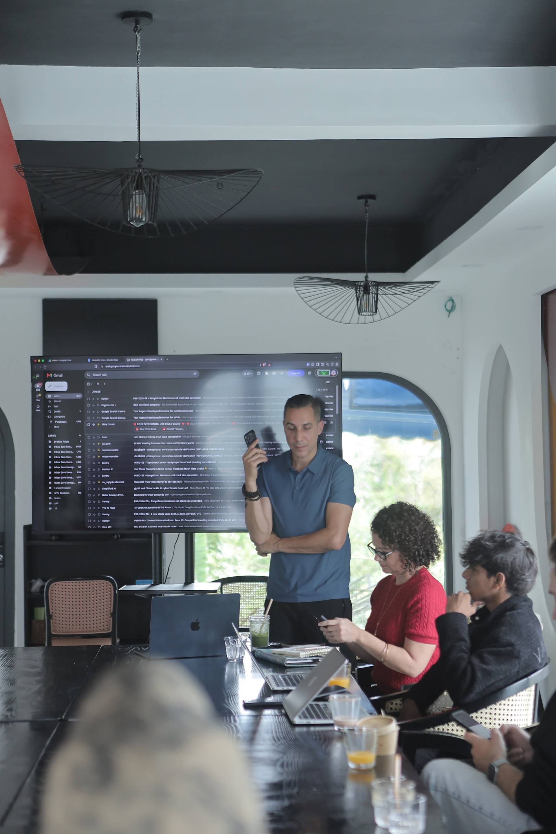 A modern office setting in Đà Lạt with a group of professionals engaged in a meeting around a large table, discussing over emails displayed on a screen.