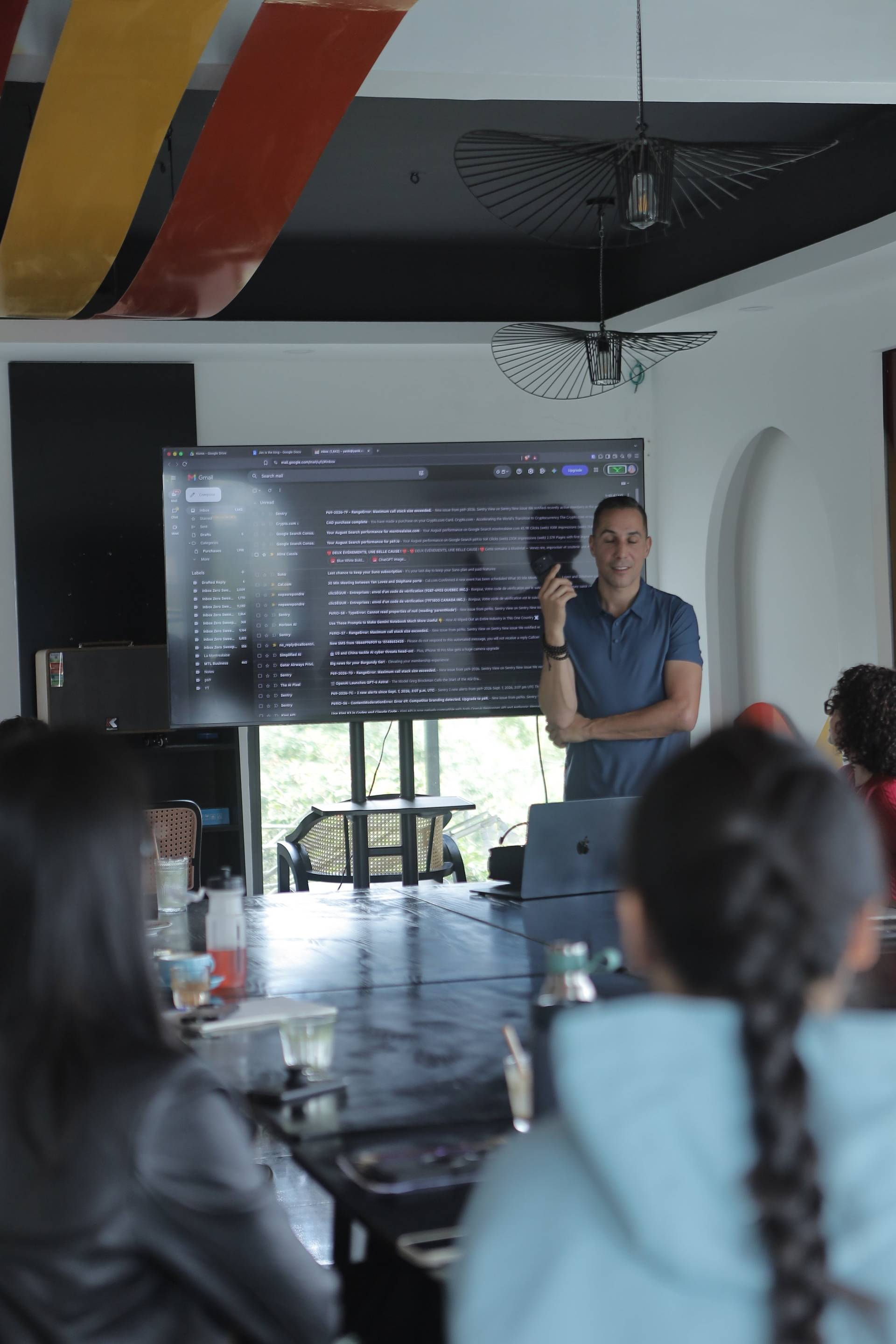A professional presentation in a modern conference room with attendees focused on the speaker and large screen displaying email content.