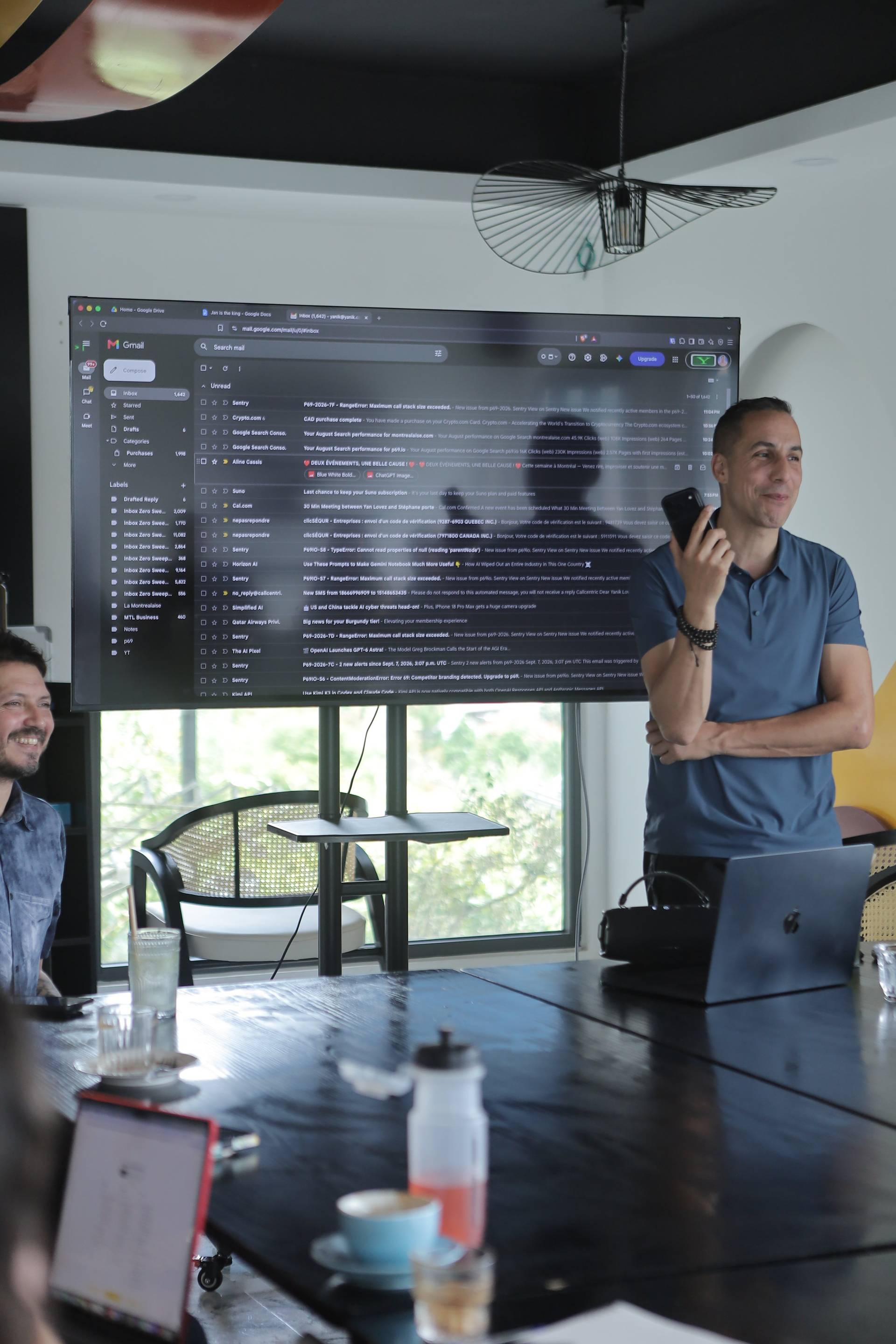 A professional meeting in a modern office space with attendees engaged in discussion, featuring a large screen displaying email content and a relaxed atmosphere.