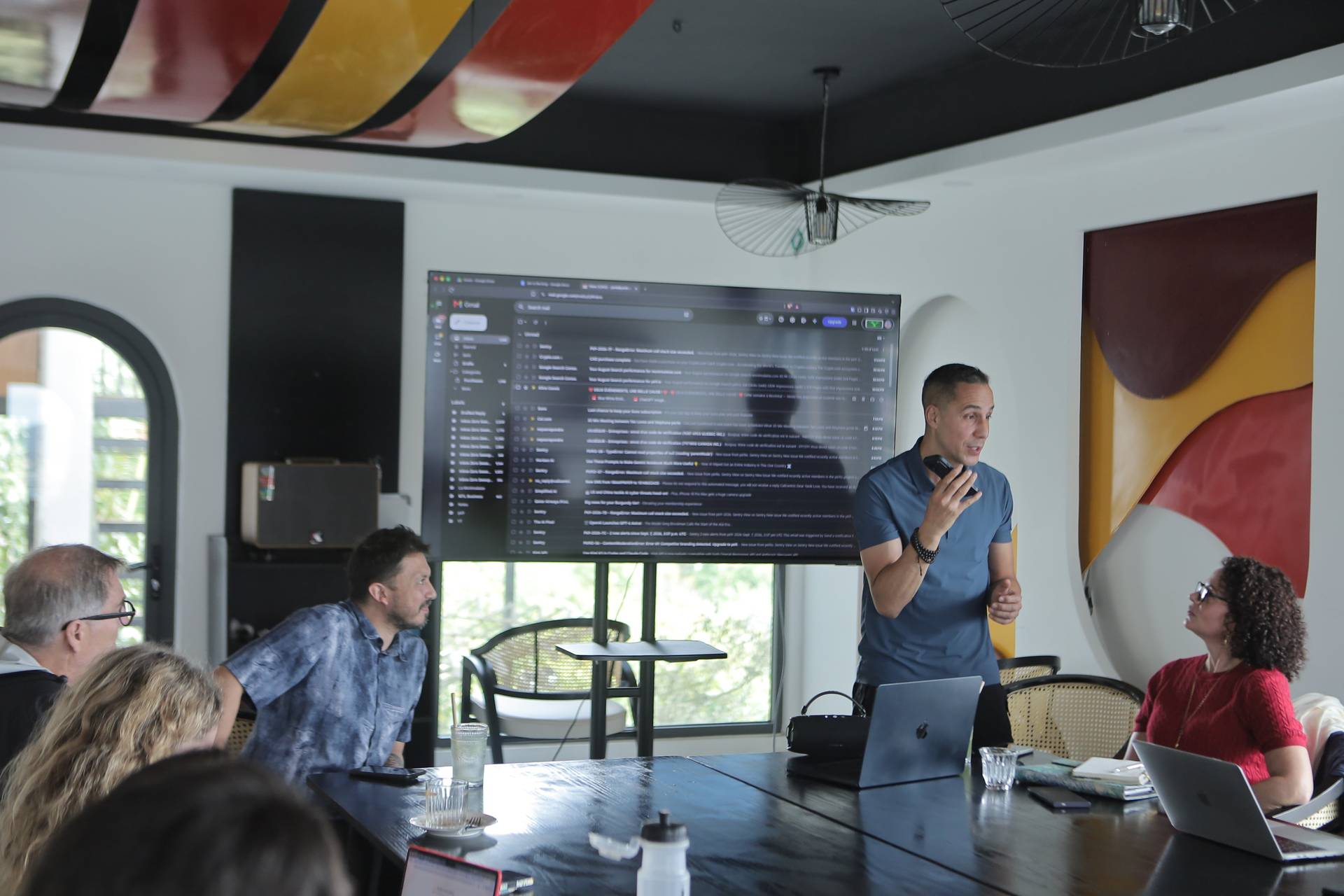 A professional meeting in a modern office space with attendees engaged in discussion around a large screen displaying email content.