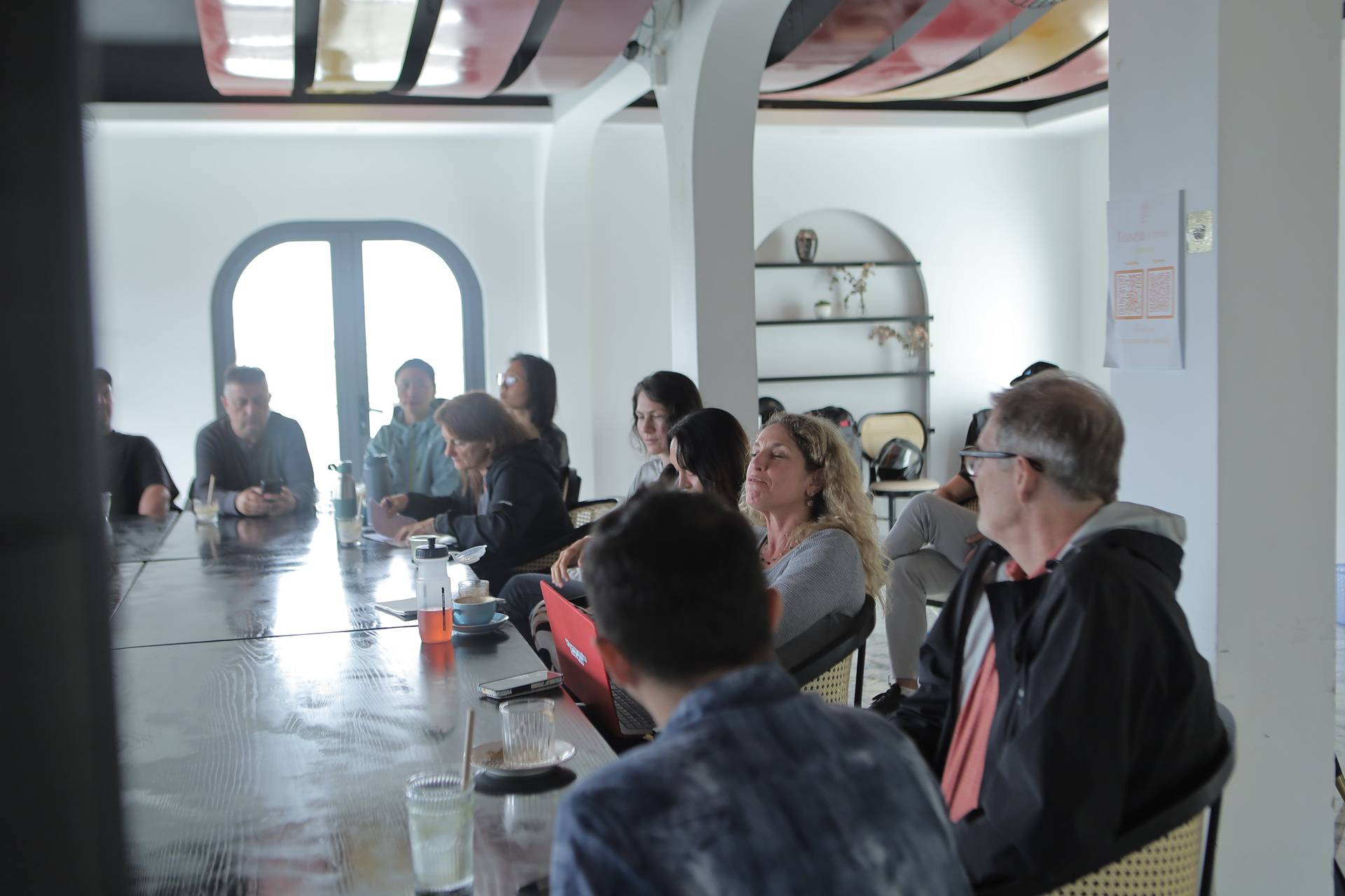 A group of people is gathered around a long table in a modern café setting in Đà Lạt, Vietnam, engaged in what appears to be a discussion or meeting with laptops and refreshments on the table.