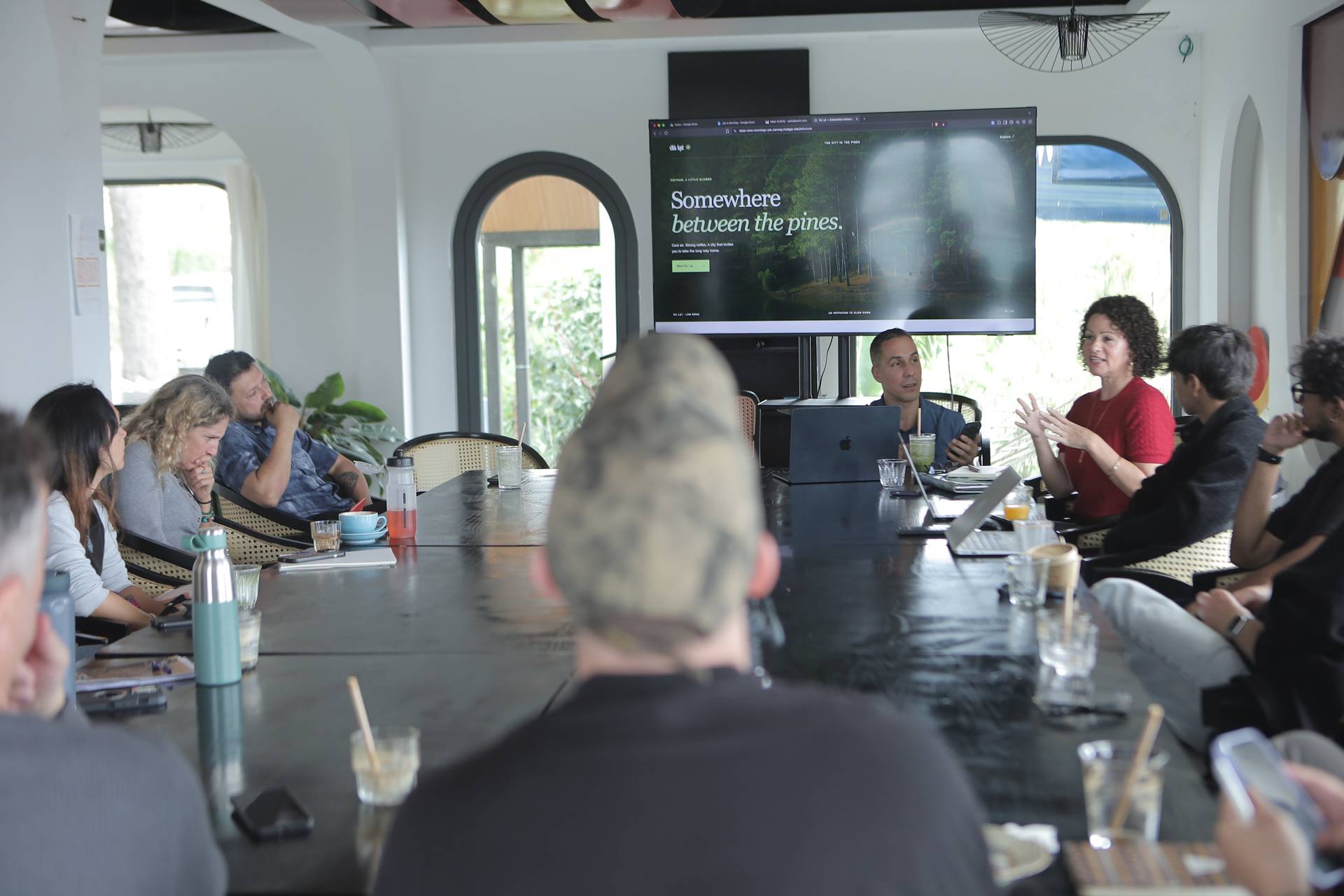 A group of people is gathered around a large table in a modern conference room in Đà Lạt, Vietnam, discussing and presenting ideas related to local tourism with a focus on pine forests.