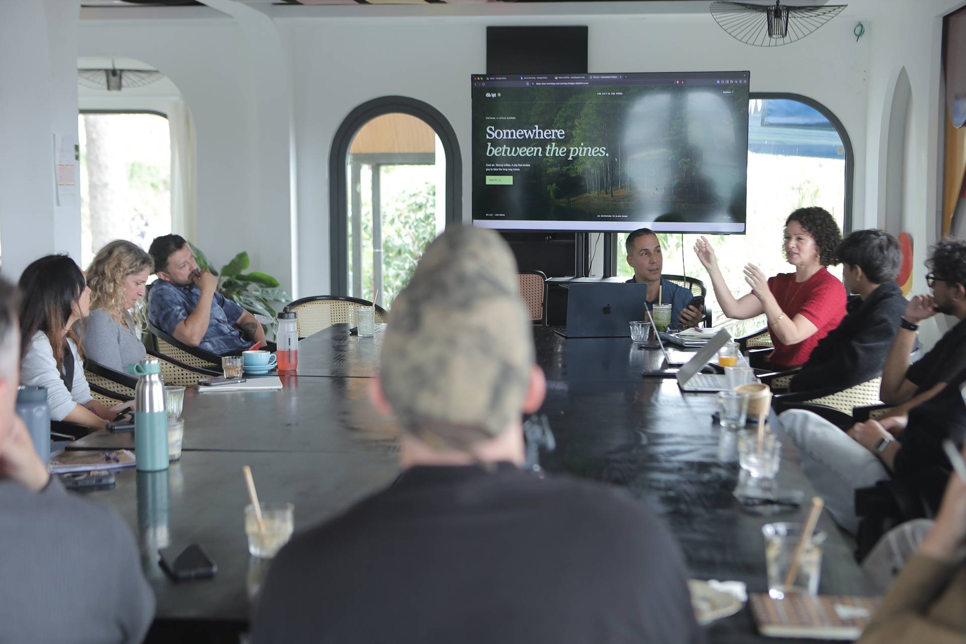 A group of professionals discusses a tourism campaign in Đà Lạt, Vietnam, with a presentation screen showcasing pine forests and the slogan 'Somewhere between the pines.'