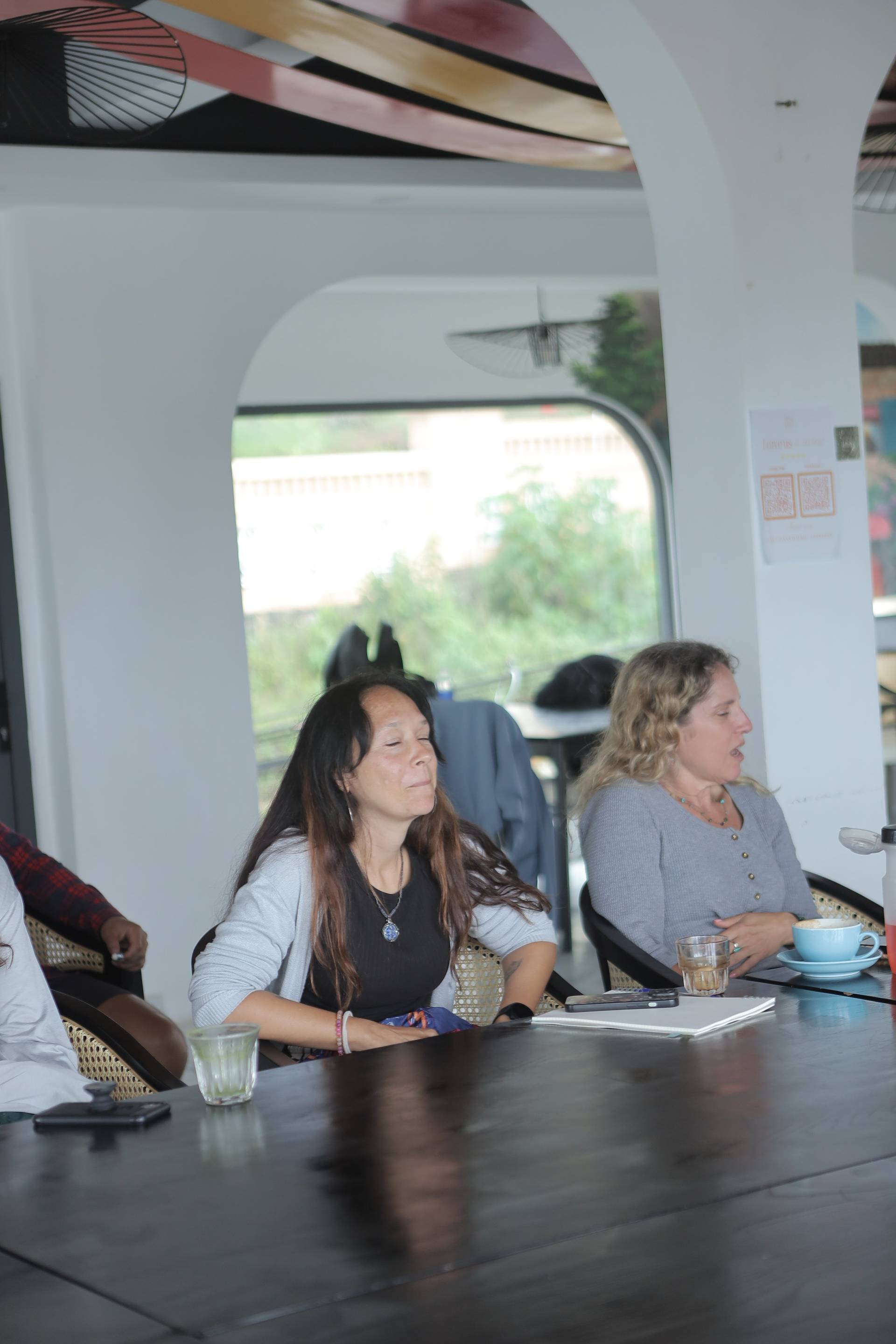 A group of people enjoying a casual gathering in a modern café with large windows overlooking Đà Lạt's scenic landscape.