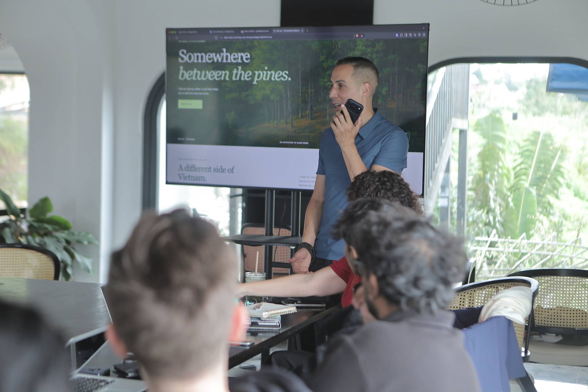 A group of people is gathered in a modern, well-lit space with large windows overlooking lush greenery, engaging in a presentation about Vietnam's natural beauty.