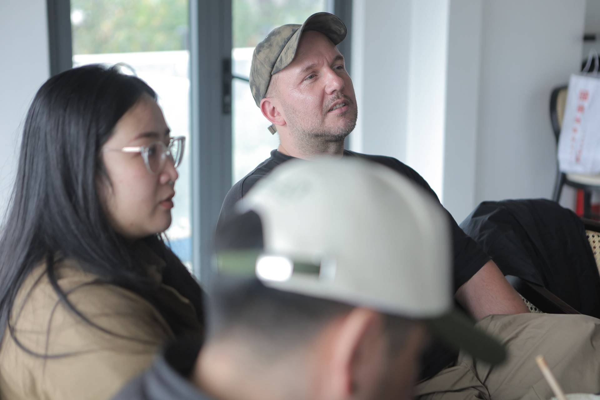 A group of individuals engaged in a discussion or meeting indoors, with one person wearing a military-style cap and another in casual attire, suggesting a collaborative or professional setting.