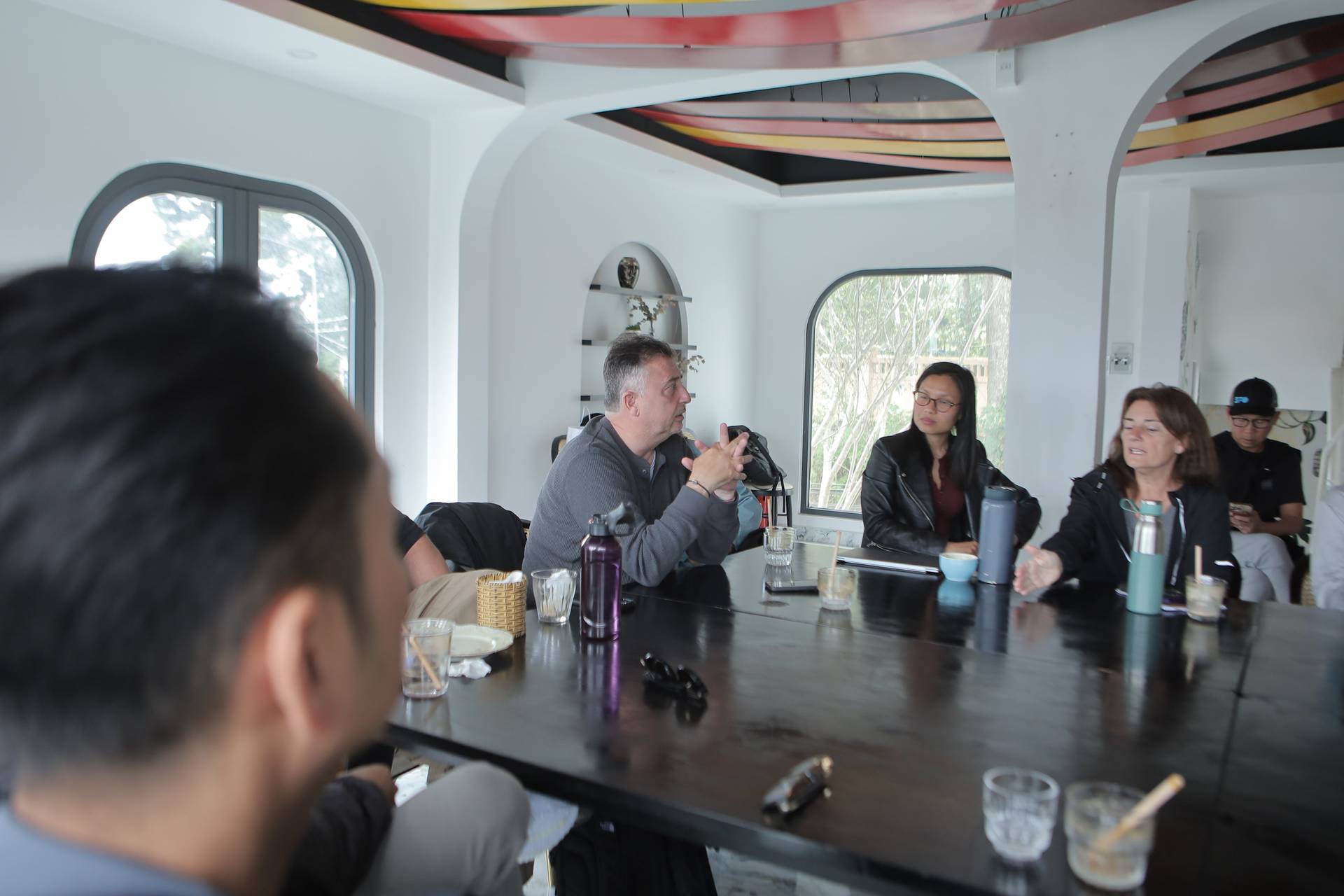 A group of people engaged in a discussion around a table in a modern café setting with large windows overlooking greenery in Đà Lạt, Vietnam.
