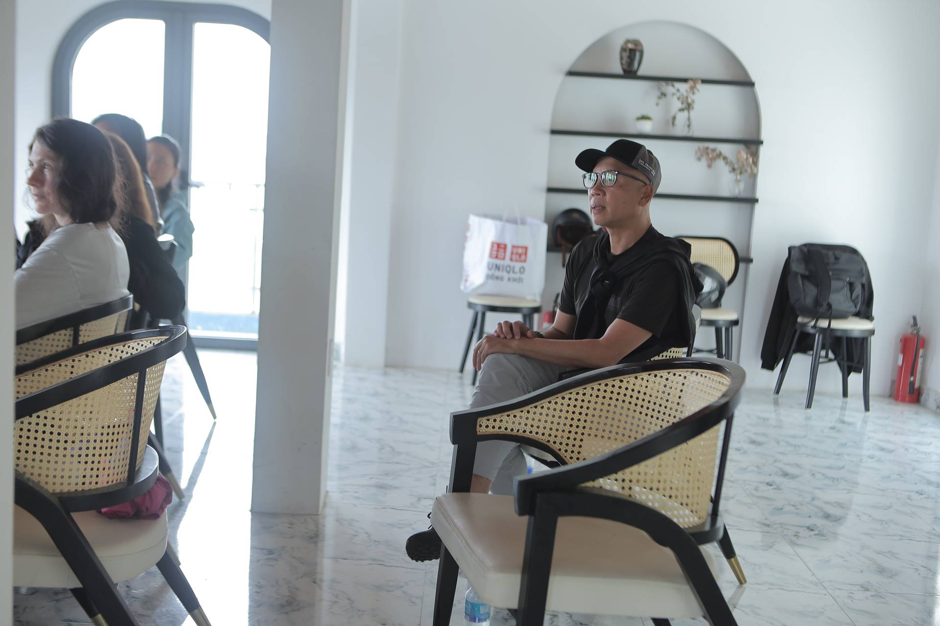 A group of attendees is seated in a modern, minimalist space with rattan chairs and white walls, likely participating in an event or presentation at a venue in Đà Lạt, Vietnam.