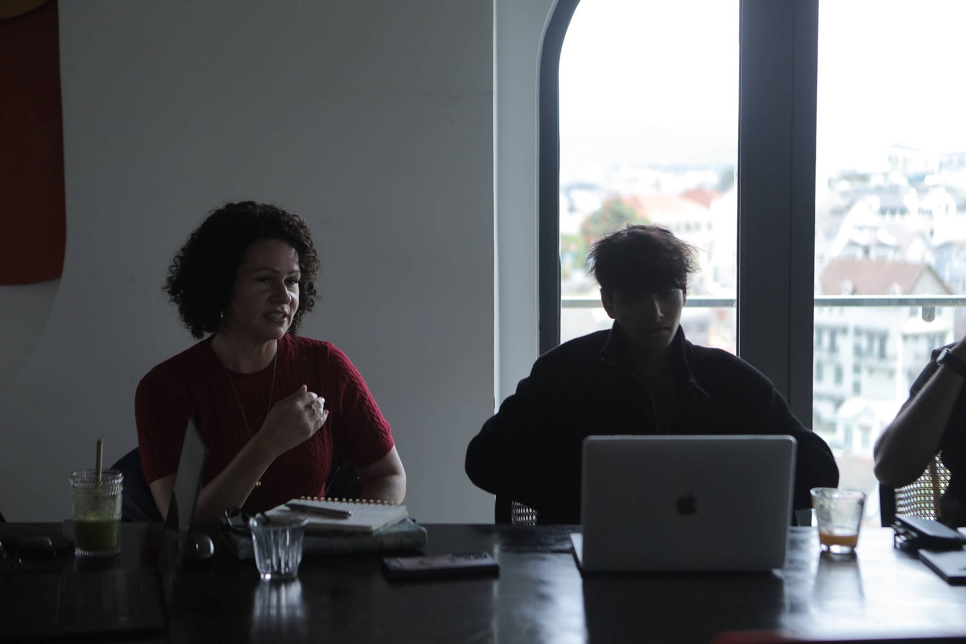 A group of individuals engaged in a discussion around a table with a laptop and drinks, set against a backdrop of large windows overlooking Đà Lạt's scenic landscape.