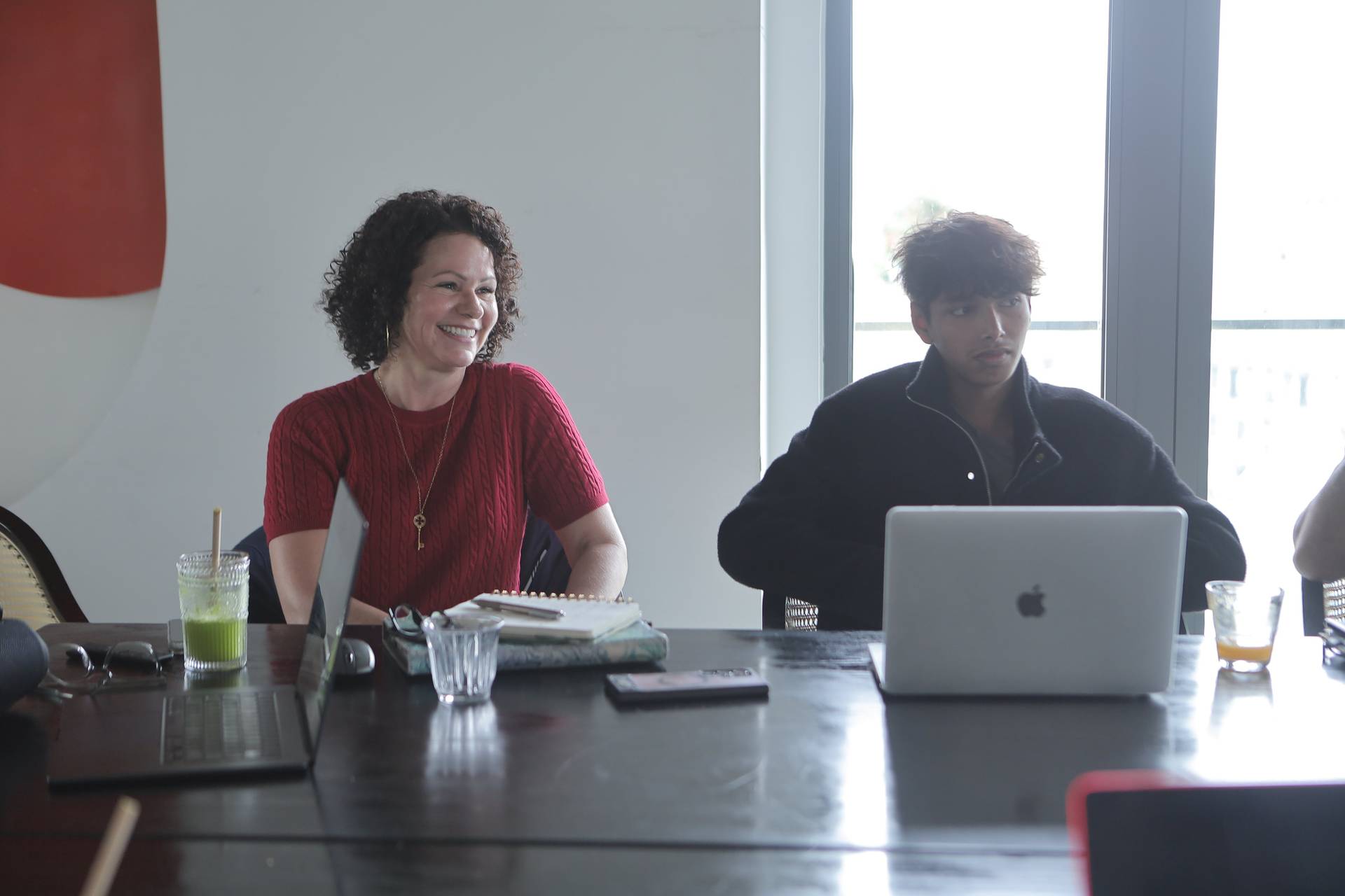 A cheerful group of individuals engaged in a collaborative meeting or workshop session in a modern Vietnamese setting, with laptops and refreshments on the table.