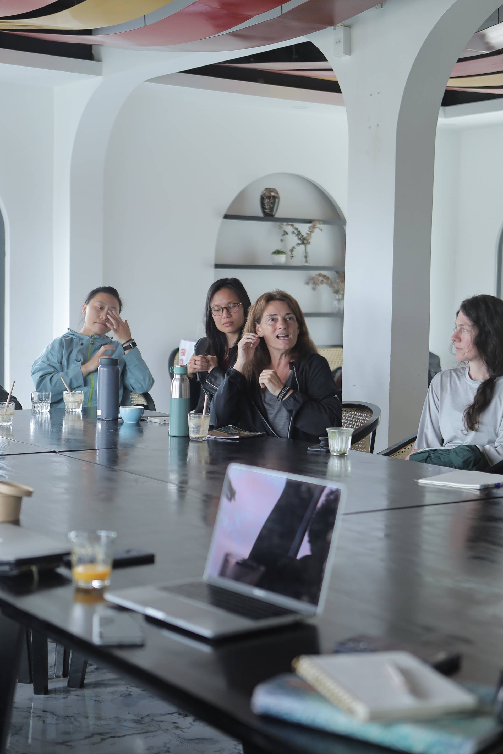 A group of individuals engaged in a discussion around a modern table setup with laptops and beverages, suggesting a collaborative or brainstorming session in a contemporary setting.