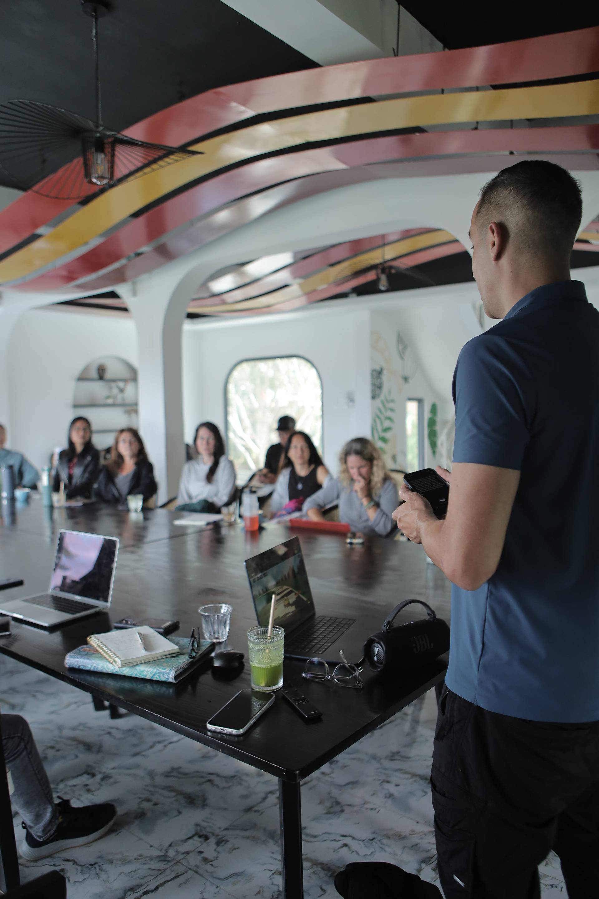 A man presents to a small audience in a modern, colorful café setting with vibrant decor and contemporary furniture.