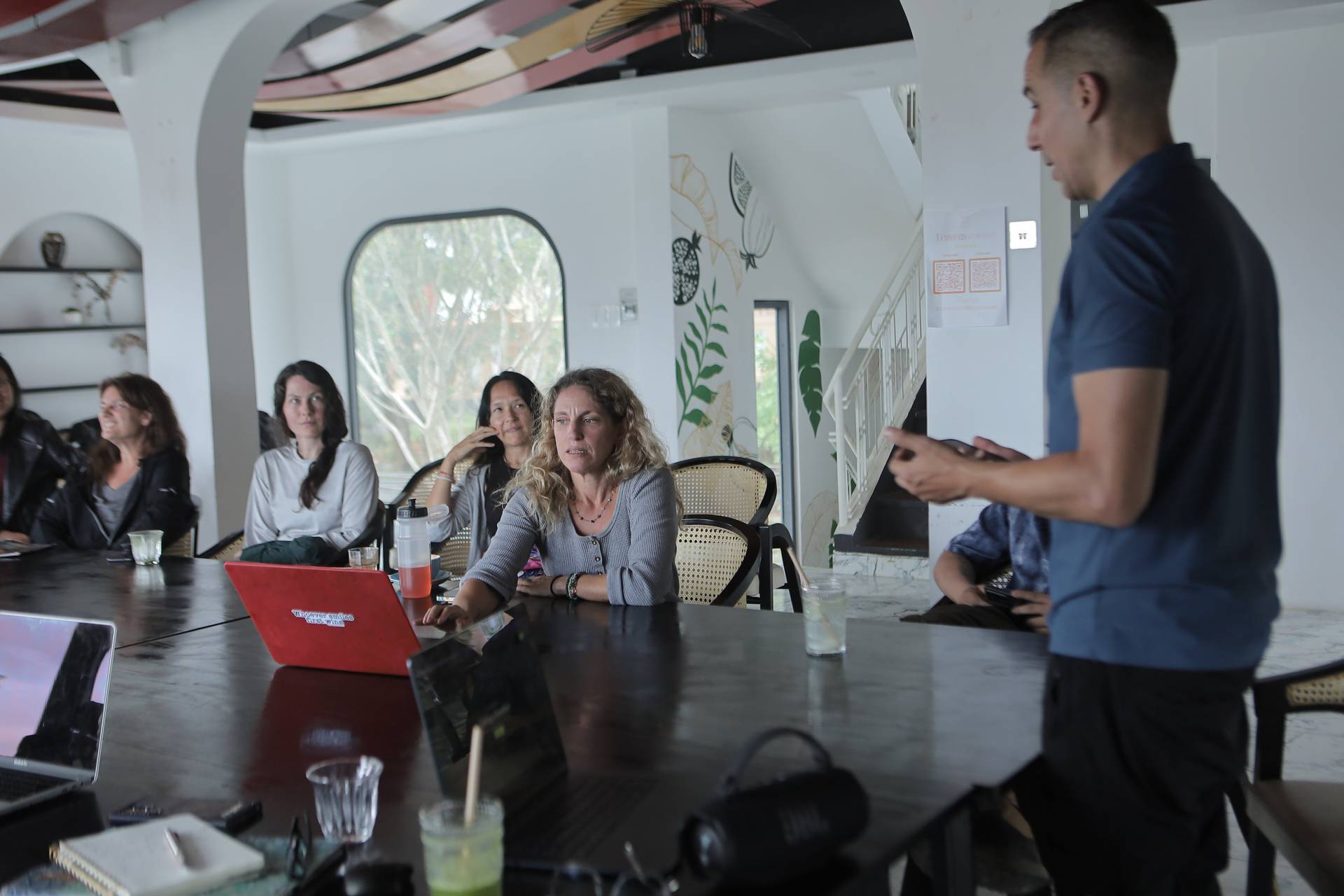 A group of people is gathered in a modern café in Đà Lạt, Vietnam, participating in a presentation or workshop led by an individual standing at the front.