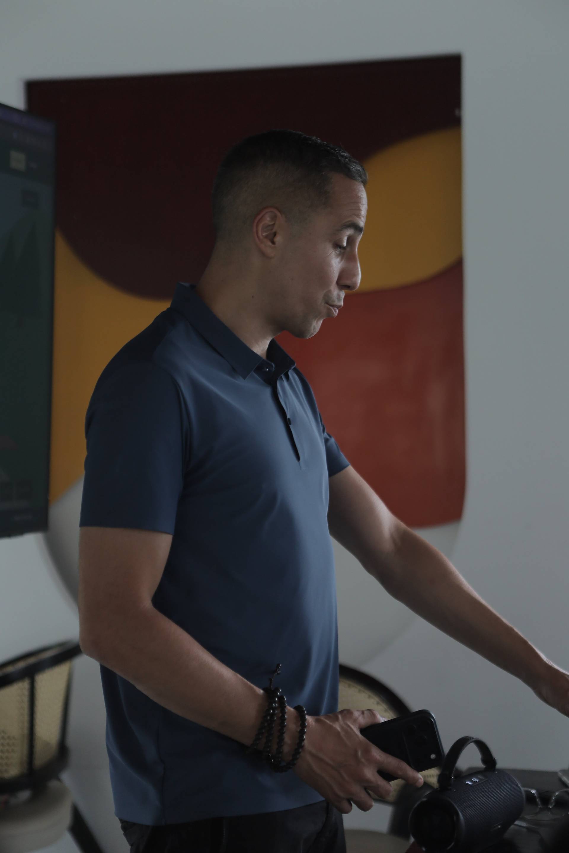 A man in a casual setting in Đà Lạt, Vietnam, holding a smartphone and interacting with a speaker, suggesting a relaxed or social event.