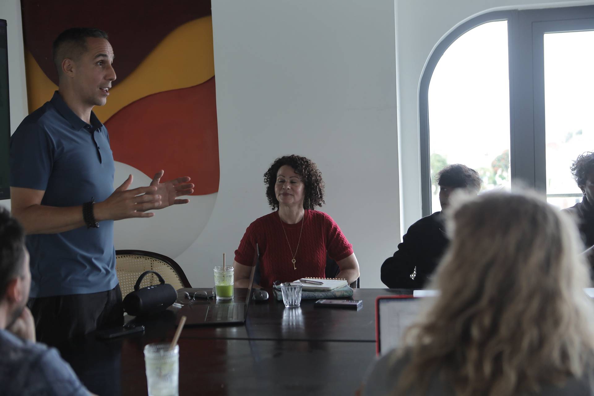 A group of people is engaged in a discussion around a table in a modern office setting with large windows overlooking Đà Lạt's scenic landscape.