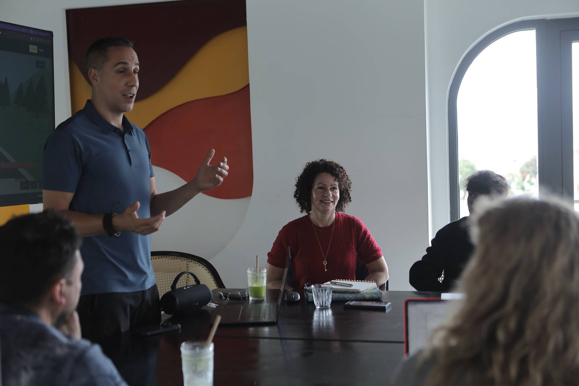 A professional meeting in a modern office space with participants engaged in discussion around a conference table.