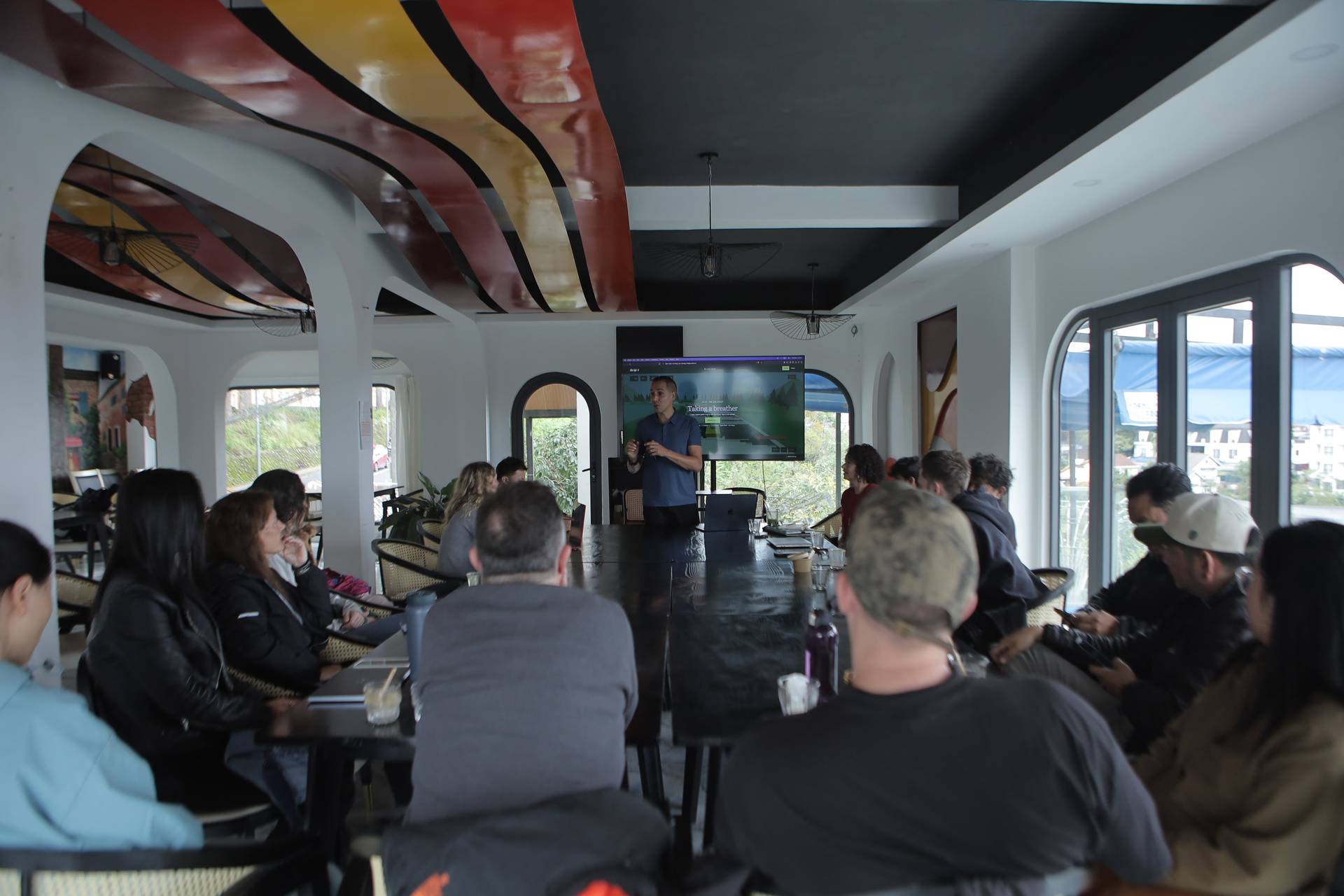 A group of people is gathered in a modern conference room in Đà Lạt, Vietnam, listening to a presentation displayed on a large screen.
