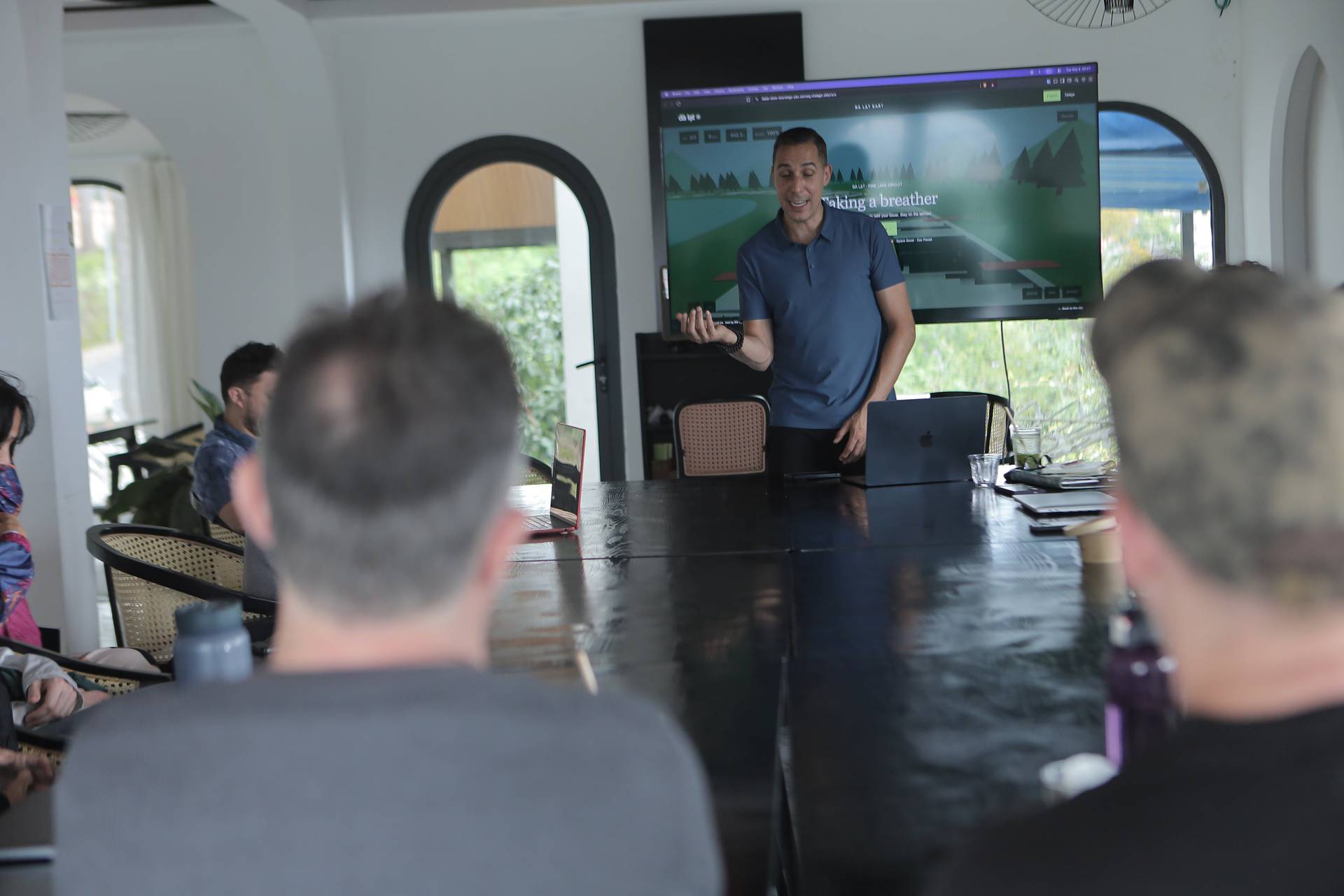 A professional presentation in a modern conference room with attendees focused on a large screen displaying a scenic image of Đà Lạt, Vietnam.