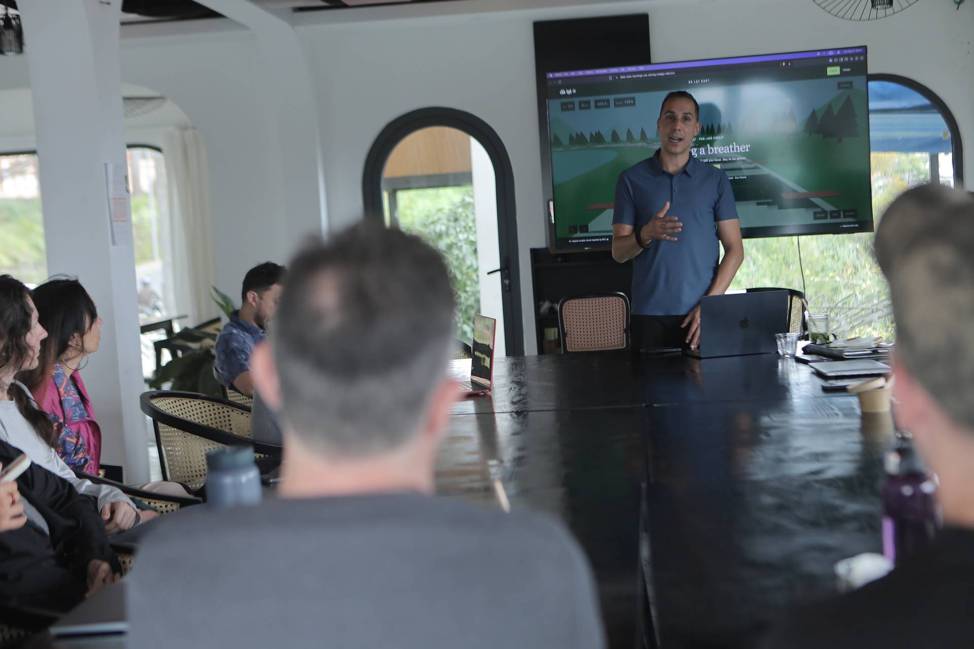 A professional presentation in a modern conference room with attendees focused on the speaker and large screen display.