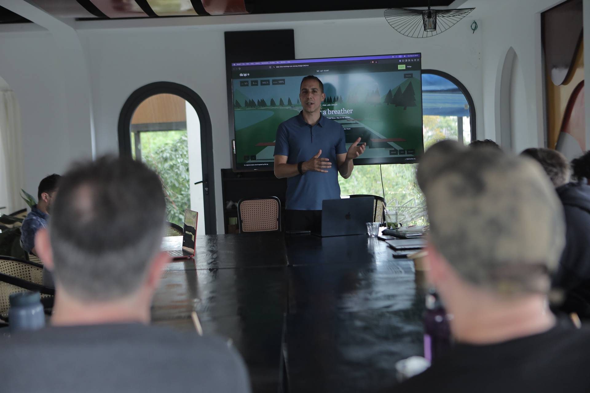 A professional presentation in a modern conference room in Đà Lạt, Vietnam, featuring a speaker discussing a digital project with an audience seated around a large table.