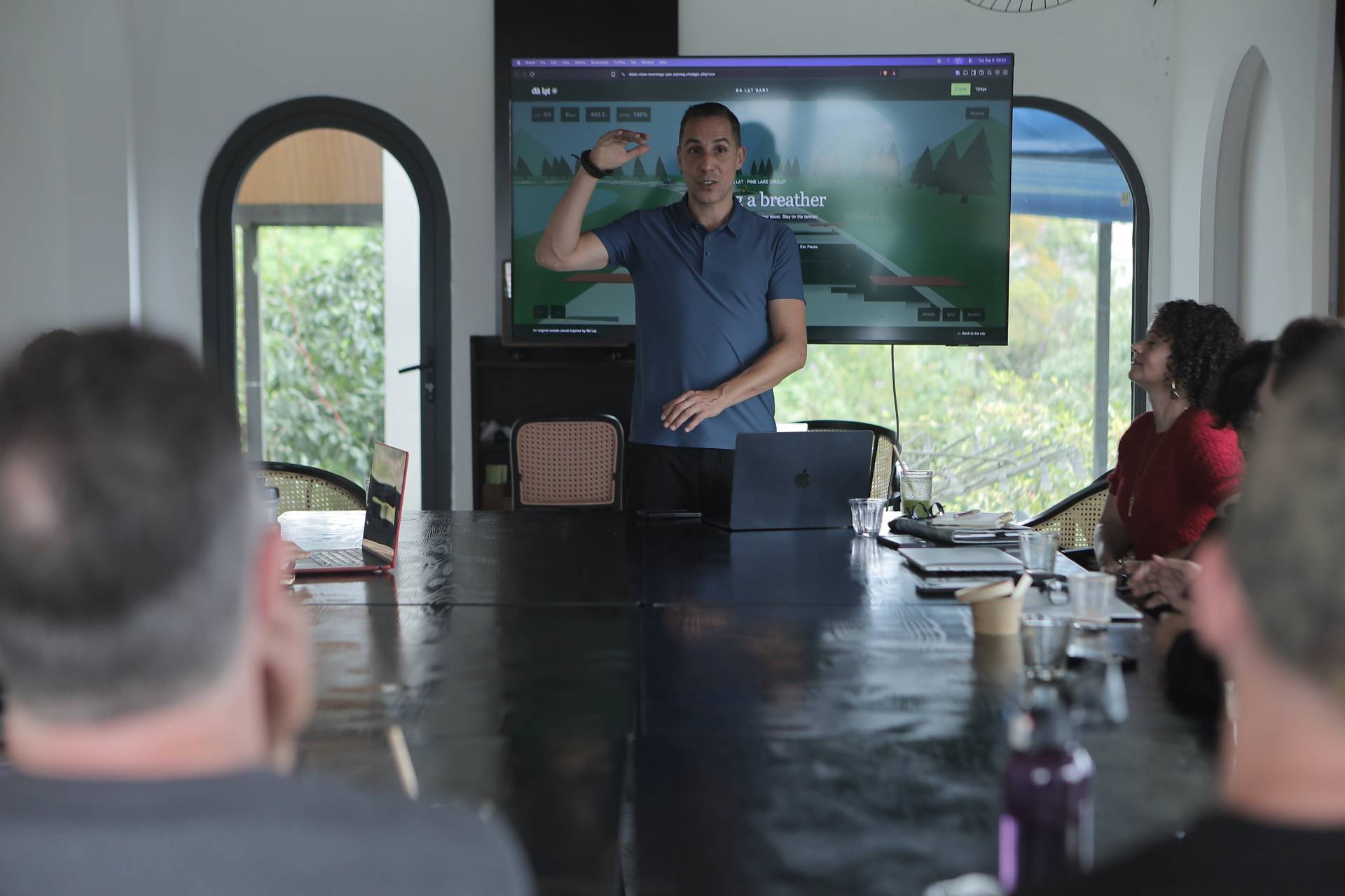 A professional presentation in a modern conference room with attendees focused on a large screen displaying a scenic image of Đà Lạt's pine forest and lake.