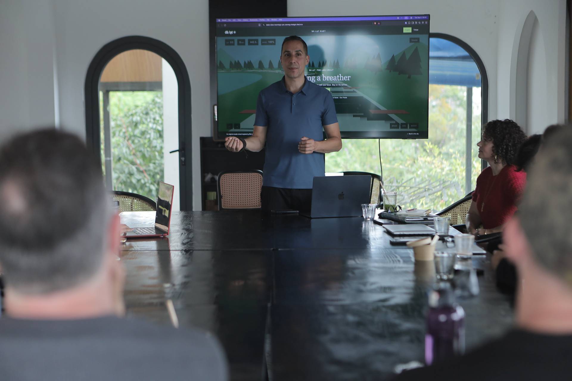 A professional presentation in a modern conference room with attendees focused on a large screen displaying a scenic image of pine trees and a road, likely part of a business or tourism event in Đà Lạt, Vietnam.