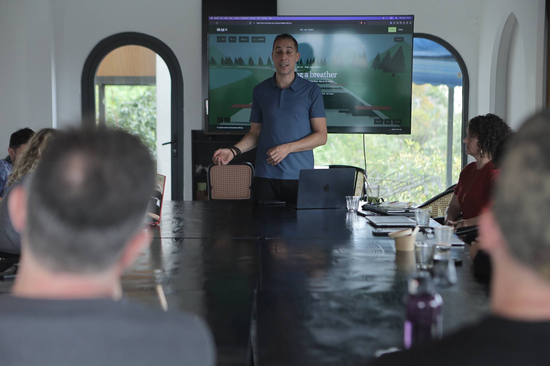 A professional presentation in a modern conference room with attendees focused on a large screen displaying a scenic route map of Đà Lạt's Pine Lake Circuit.