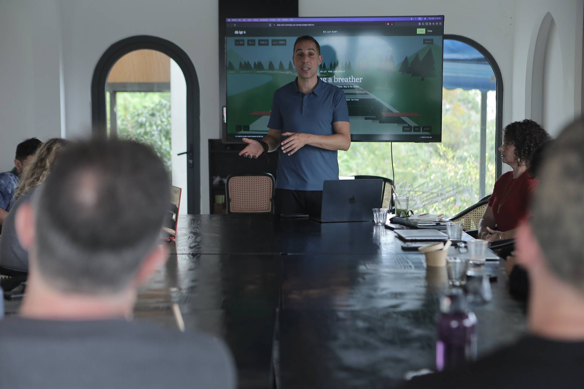 A professional presentation in a modern conference room with attendees focused on a large screen displaying a scenic image of Đà Lạt's pine forest and golf course.