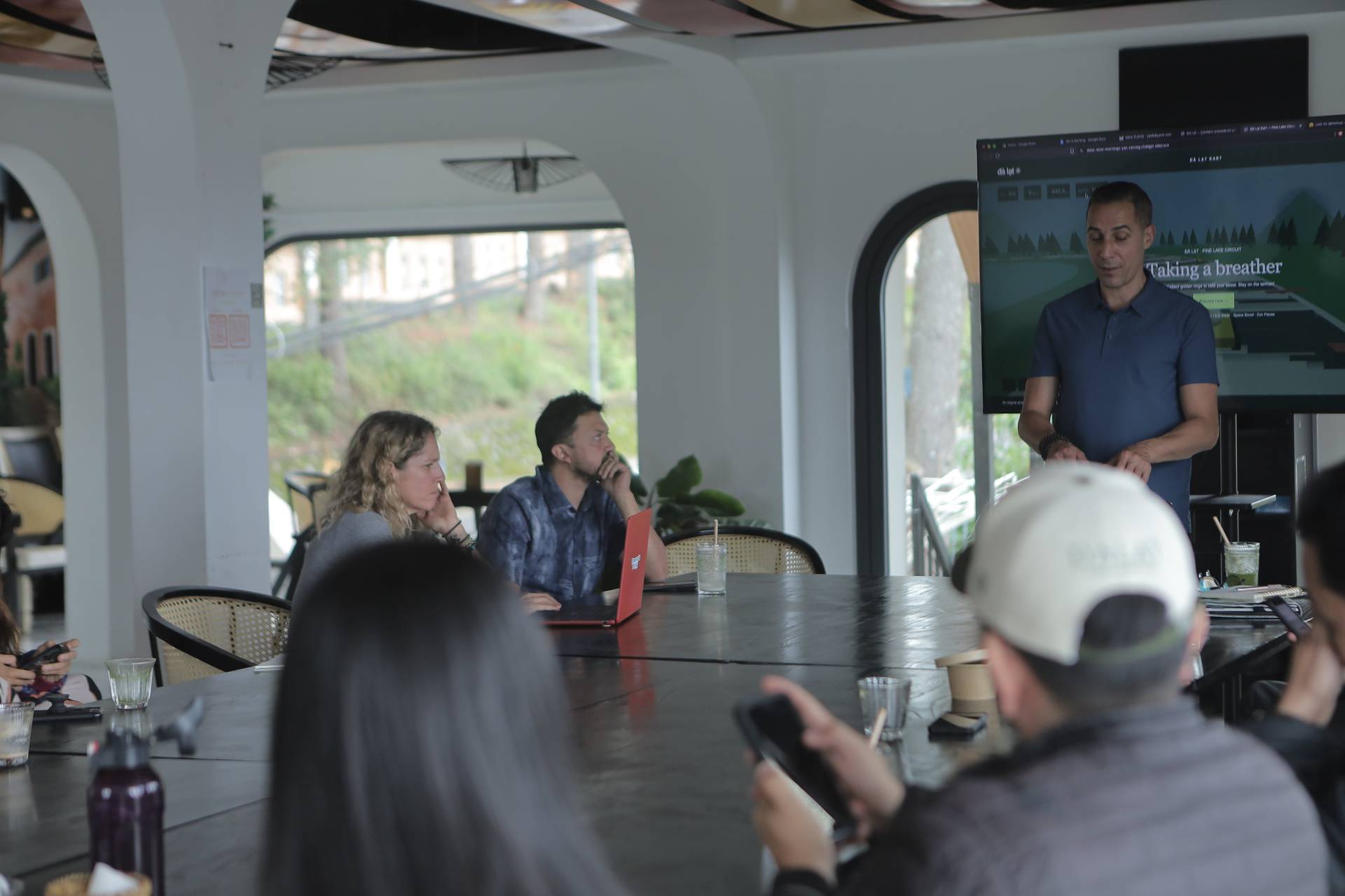 A group of people is gathered in a modern café in Đà Lạt, Vietnam, listening to a presentation about taking a break and enjoying nature.
