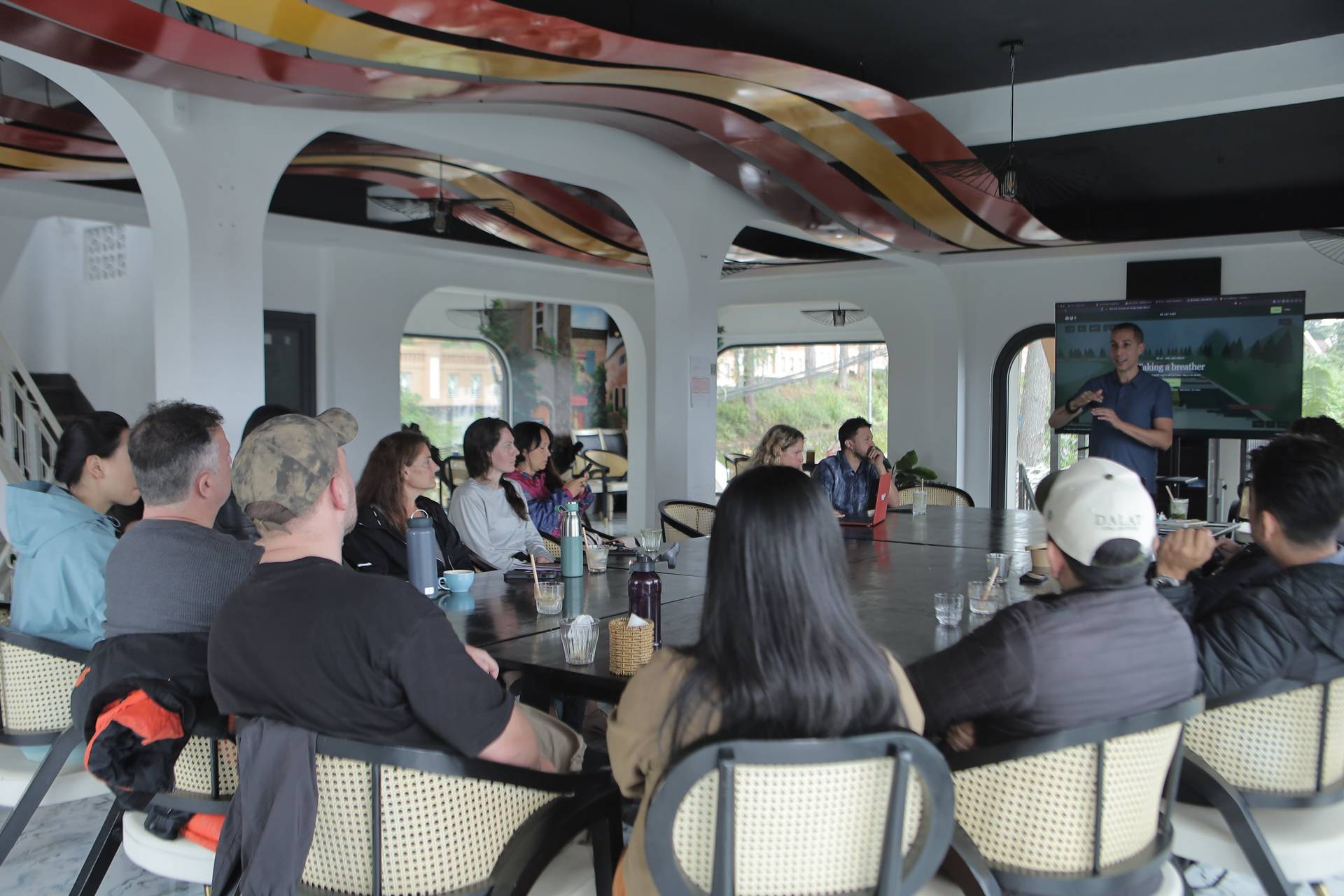 A group of people is gathered in a modern, open-air meeting space in Đà Lạt, Vietnam, attentively listening to a presentation by an individual standing at the front.