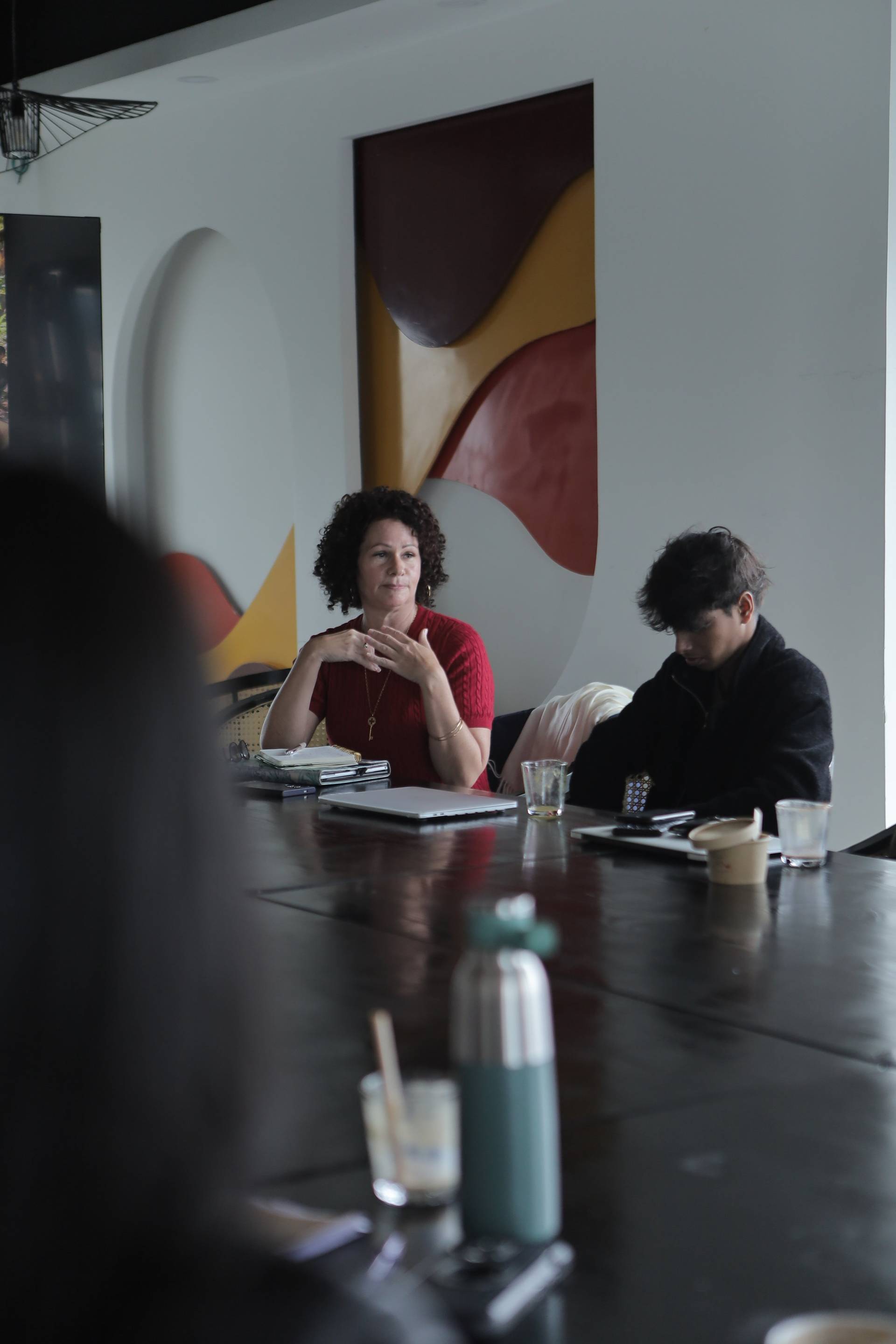 A group of individuals engaged in a meeting or discussion around a modern table in a stylish café setting with vibrant abstract art in the background.