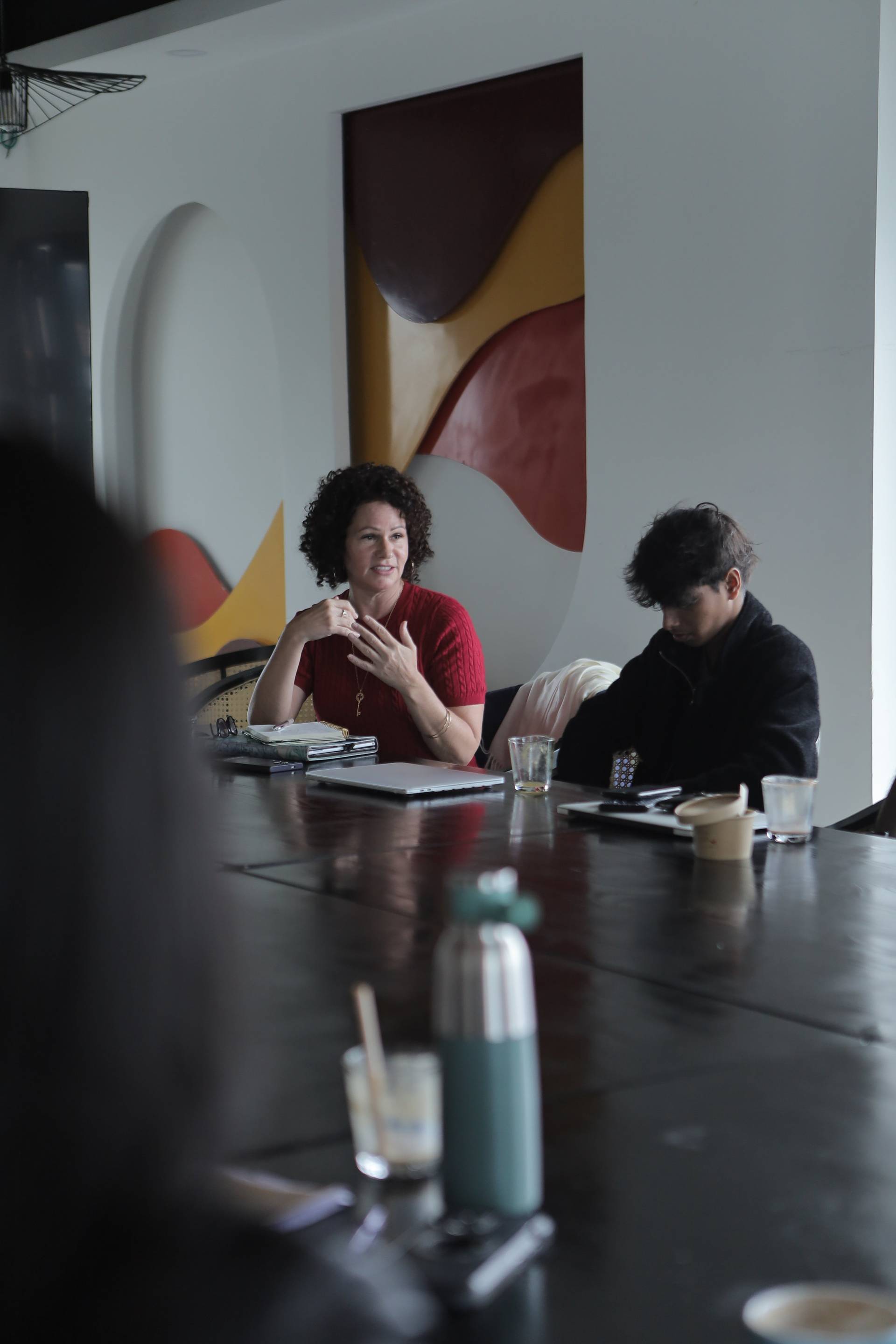 A professional meeting in a modern café setting with individuals engaged in discussion over coffee and digital devices.