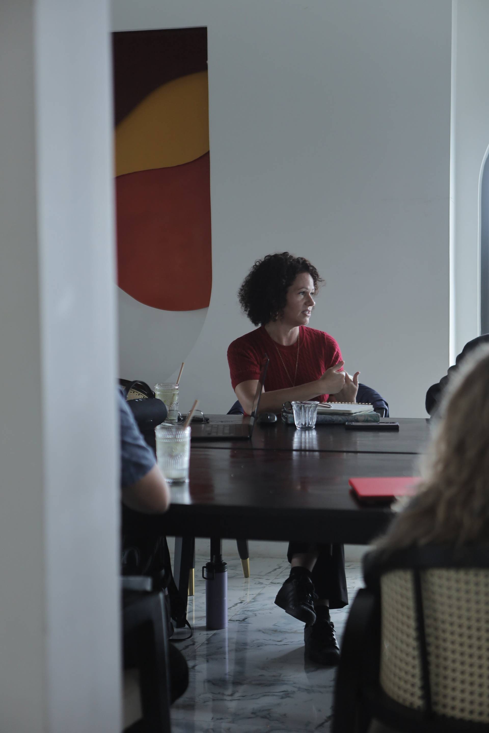 A woman in a red shirt leads a discussion during a meeting in a modern office space with colorful artwork in Đà Lạt.