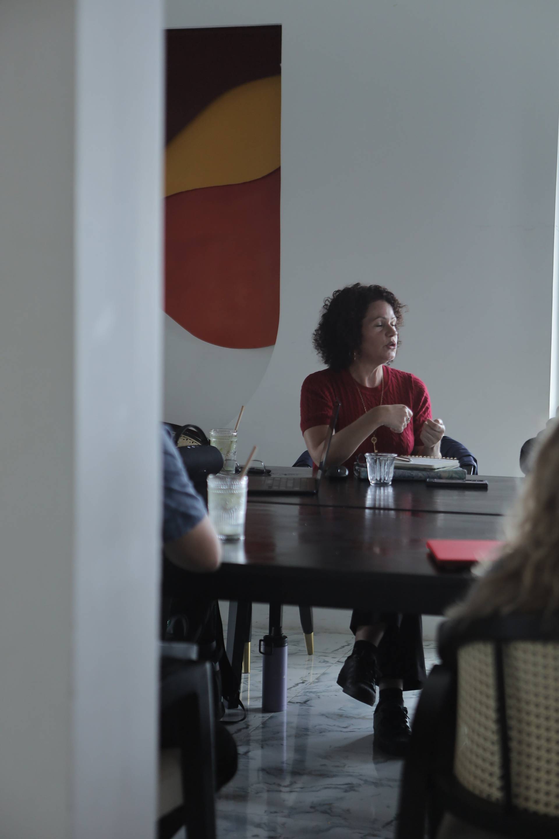 A woman in a red shirt sits at a table with drinks and a laptop, engaged in conversation or work within a modern café setting in Đà Lạt.