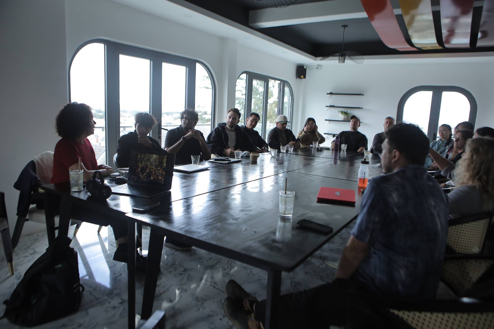 A group of people is gathered around a long table in a modern conference room with large windows overlooking Đà Lạt's scenic landscape, engaged in what appears to be a collaborative meeting or brainstorming session.