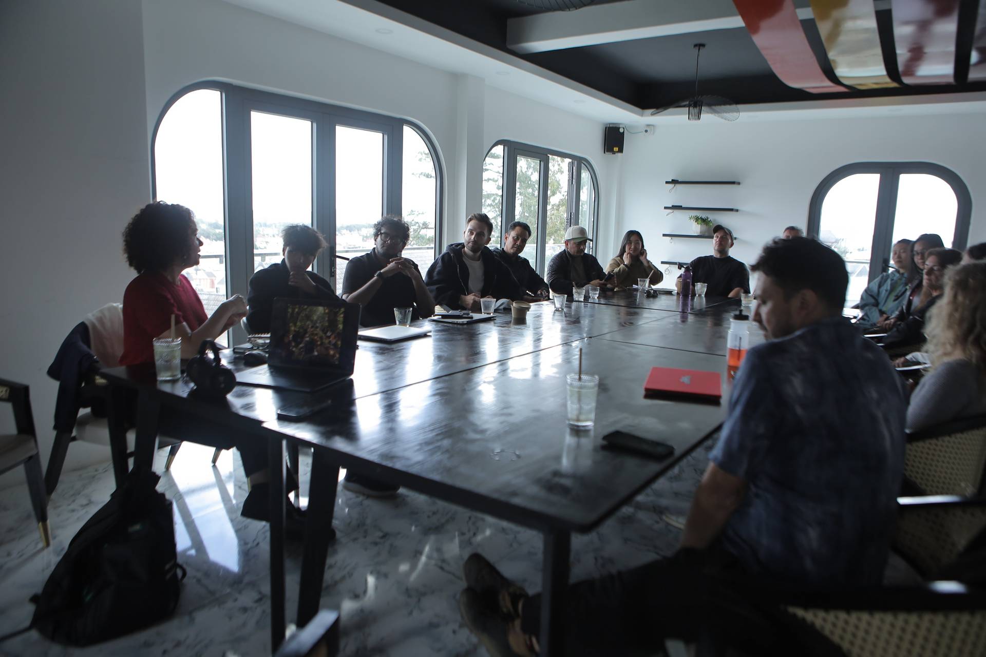 A group of people is gathered around a long table in a modern conference room with large windows overlooking Đà Lạt's scenic landscape, engaged in what appears to be a professional or collaborative meeting.