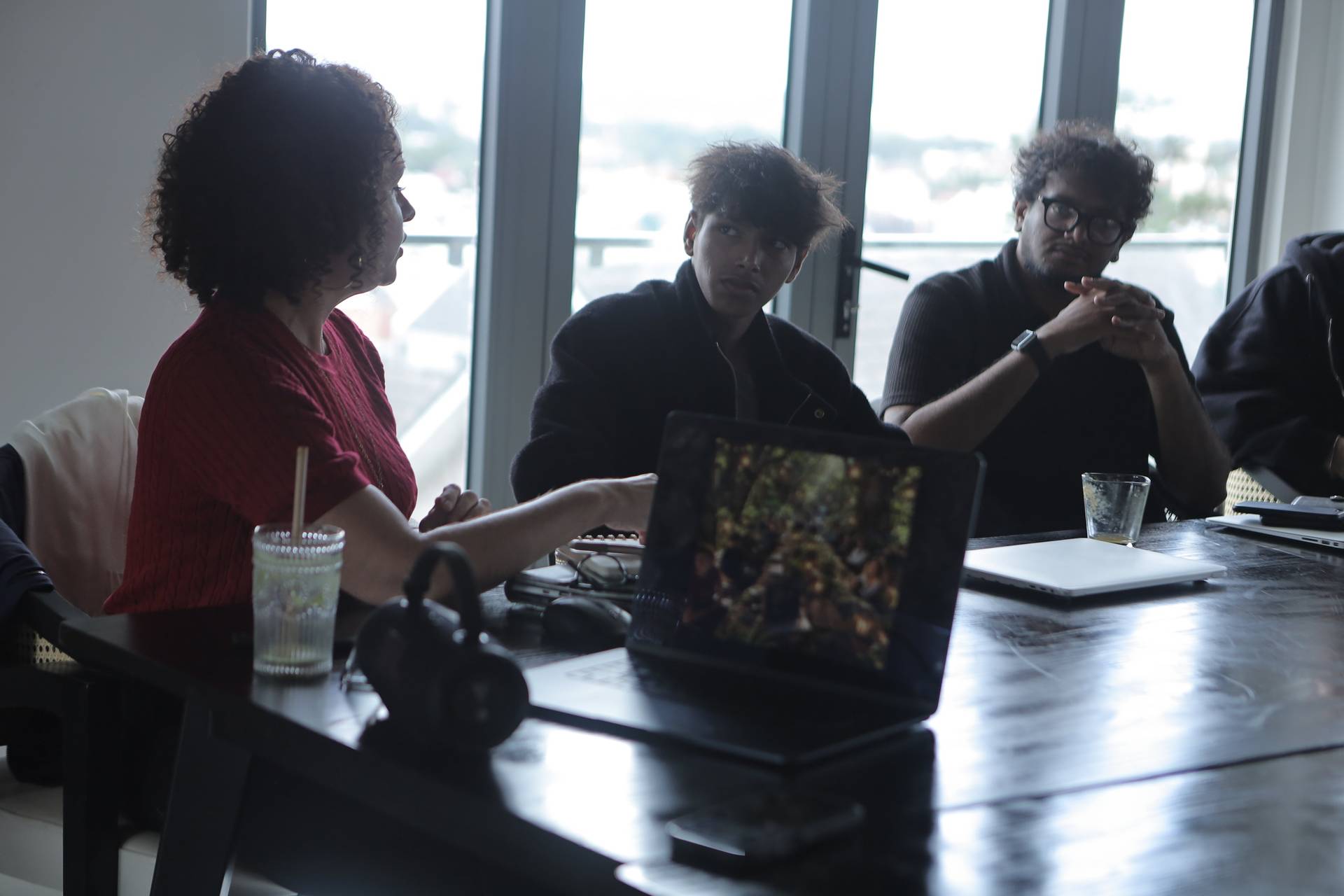 A group of friends engaged in a discussion around a table with laptops and drinks, set against large windows overlooking Đà Lạt's scenic landscape.