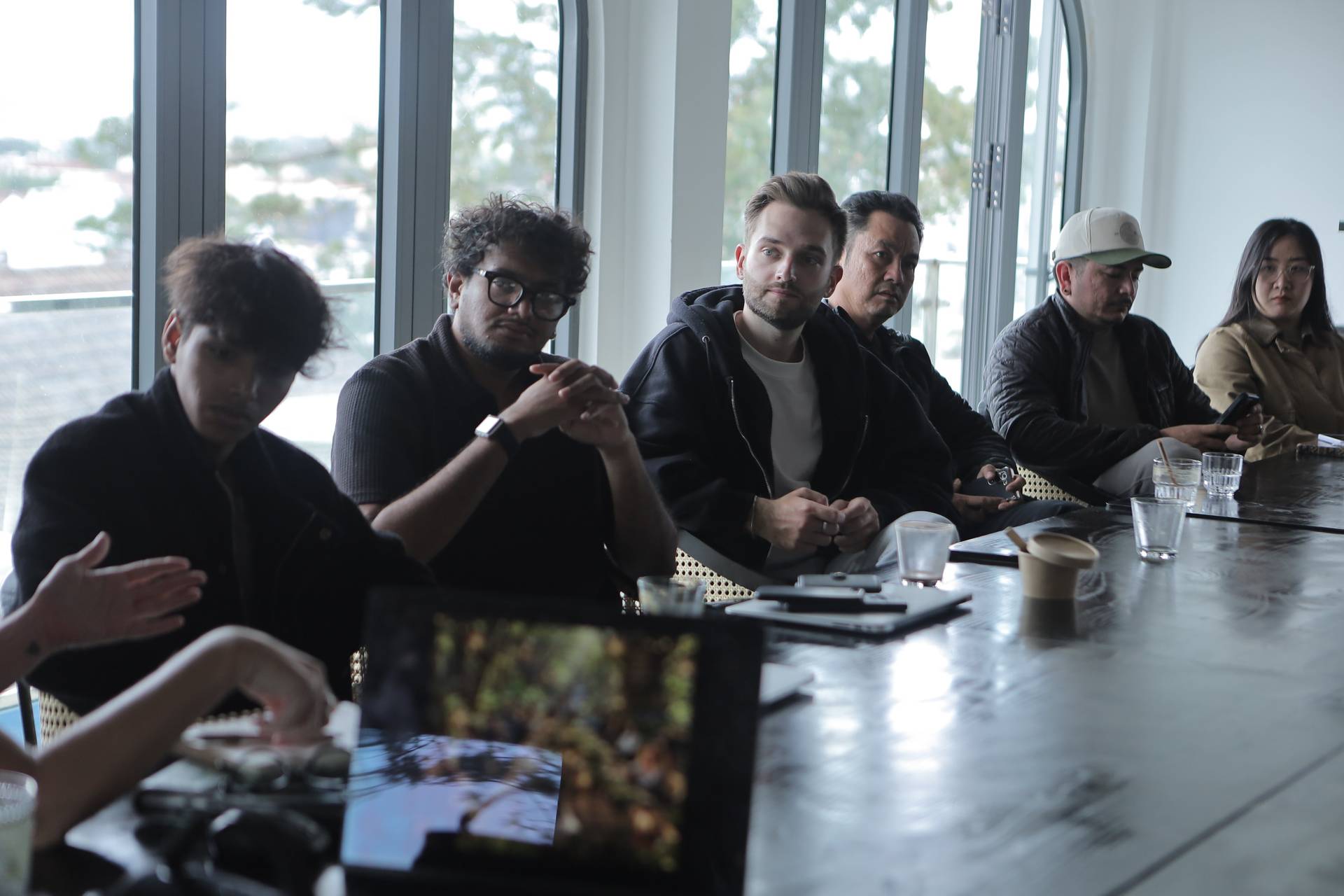 A group of individuals engaged in a discussion around a table with modern decor and large windows overlooking a scenic view in Đà Lạt, Vietnam.