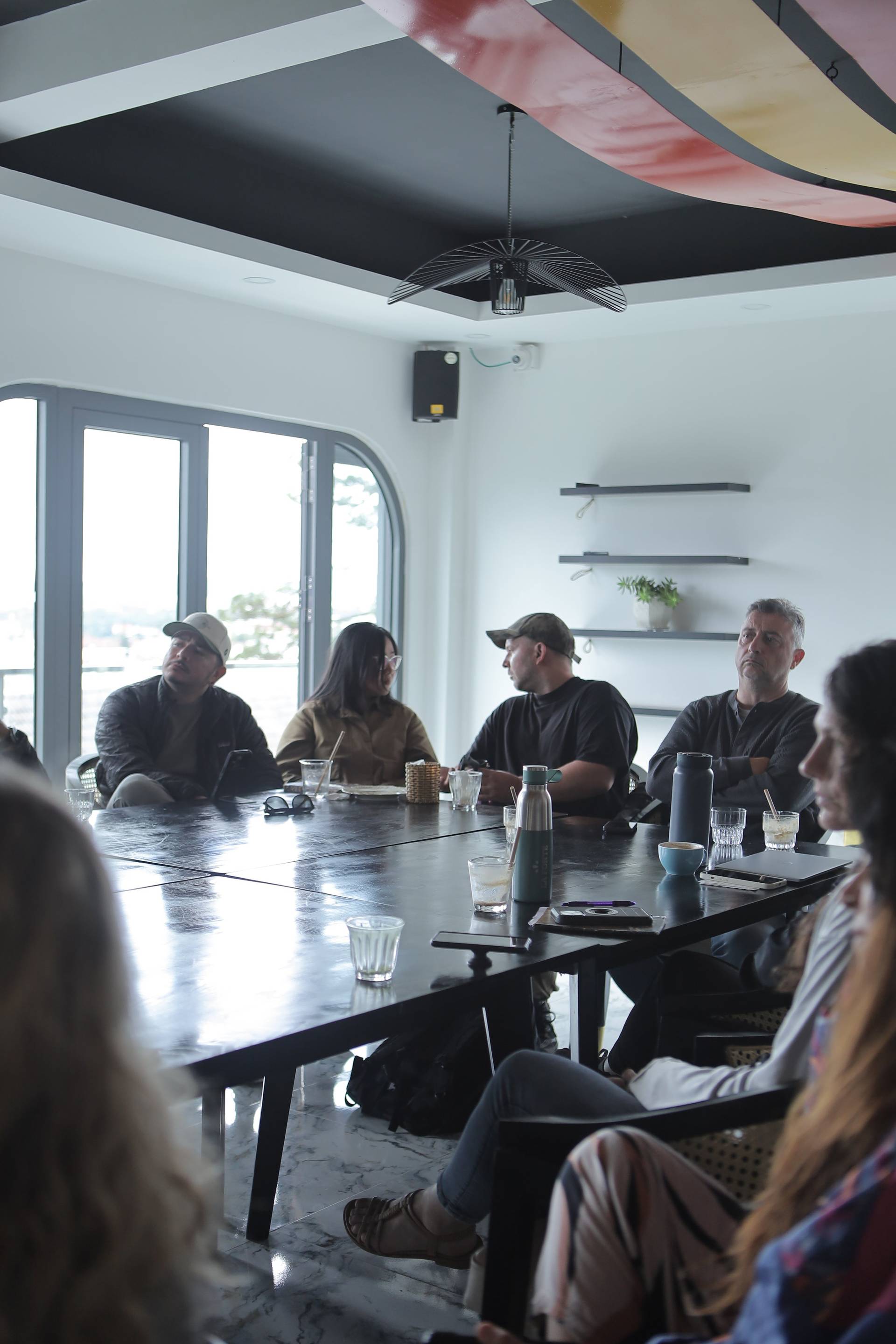 A group of people is gathered around a long table in a modern café setting in Đà Lạt, Vietnam, engaged in what appears to be a casual meeting or discussion.