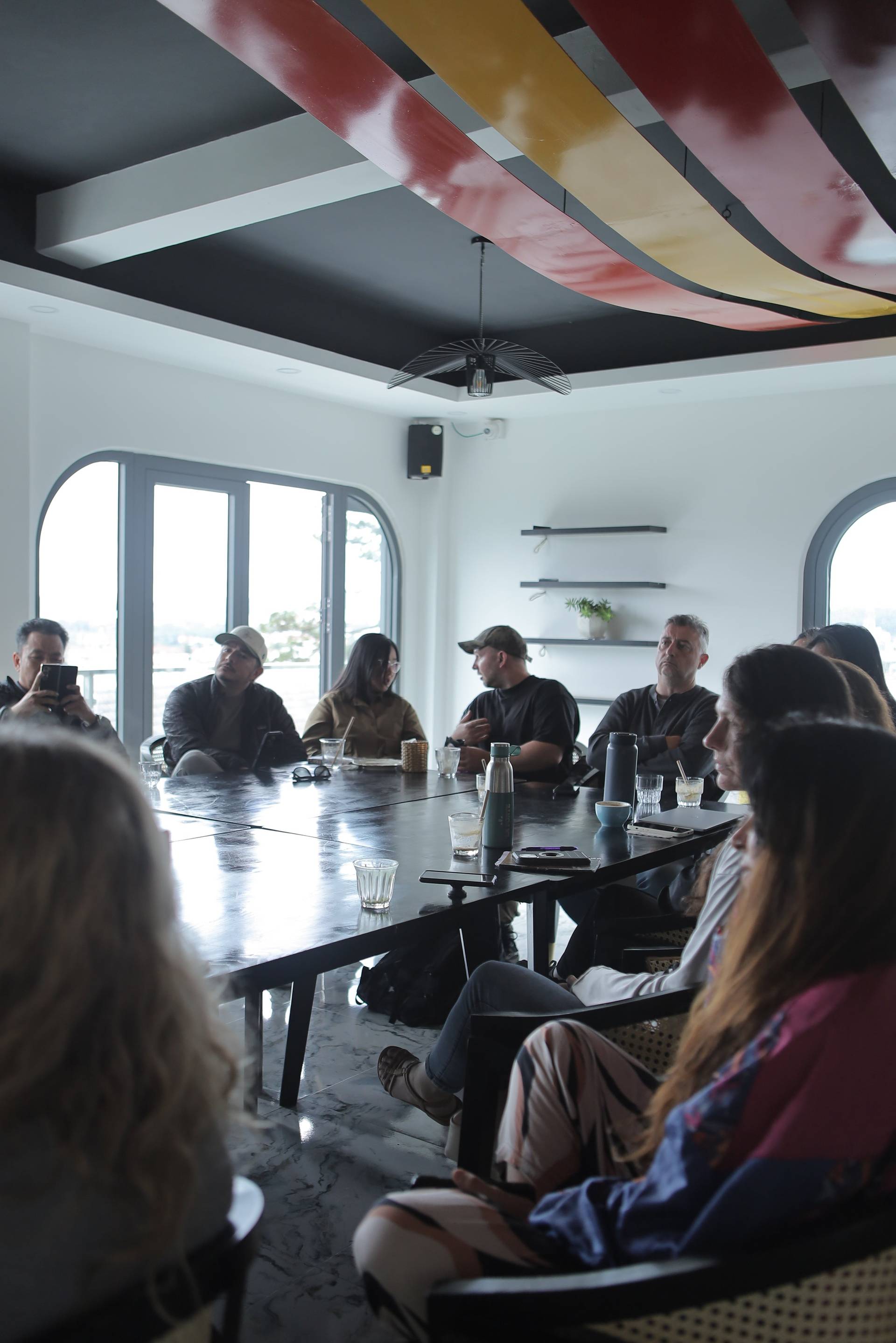 A group of people is gathered around a long table in a modern café setting in Đà Lạt, Vietnam, engaging in what appears to be a casual meeting or discussion.