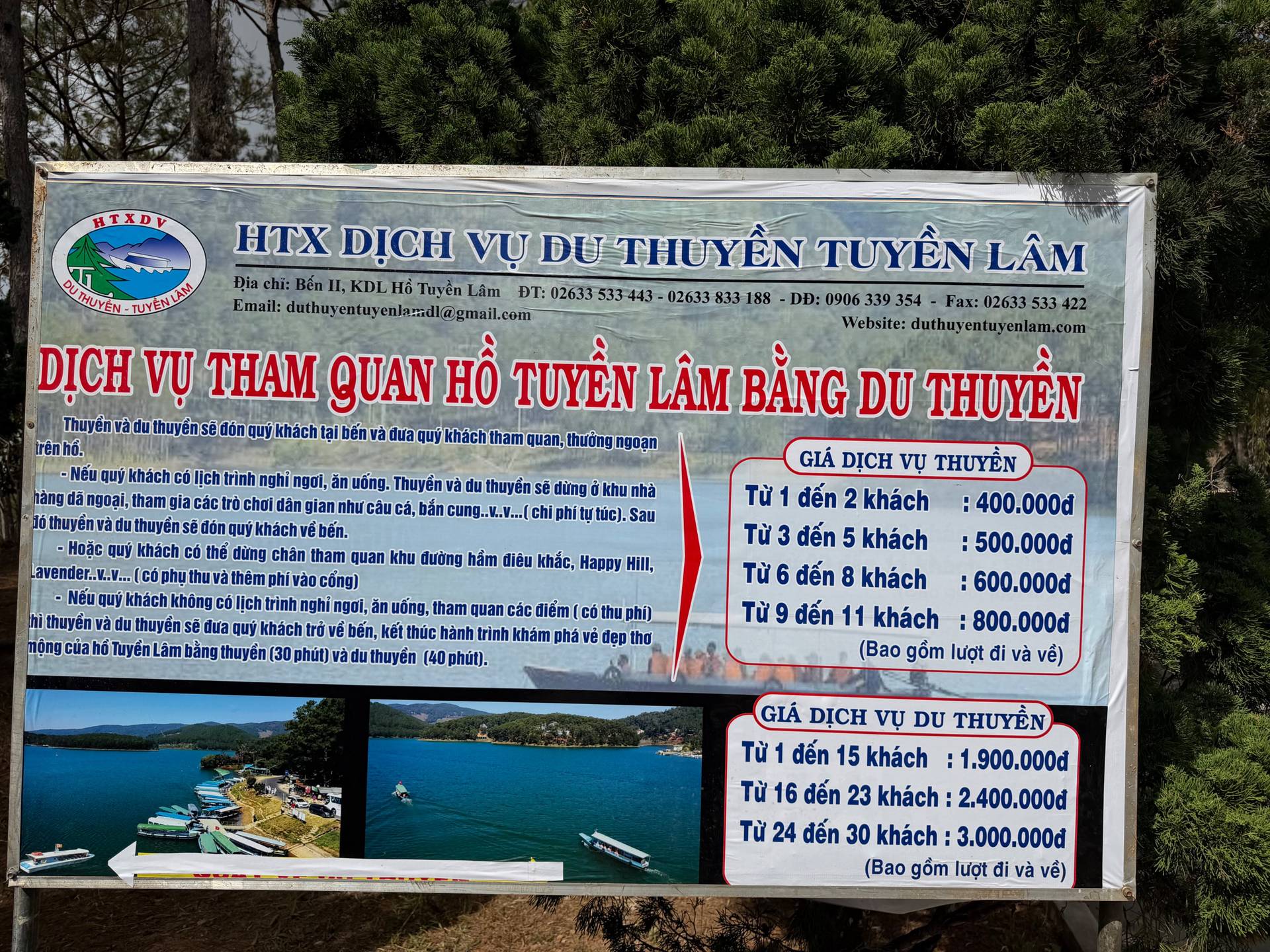A professional service sign advertises boat tours on Tuyền Lâm Lake in Đà Lạt, displaying Vietnamese pricing information and scenic photos of the waterfront. The signage offers various tour packages.