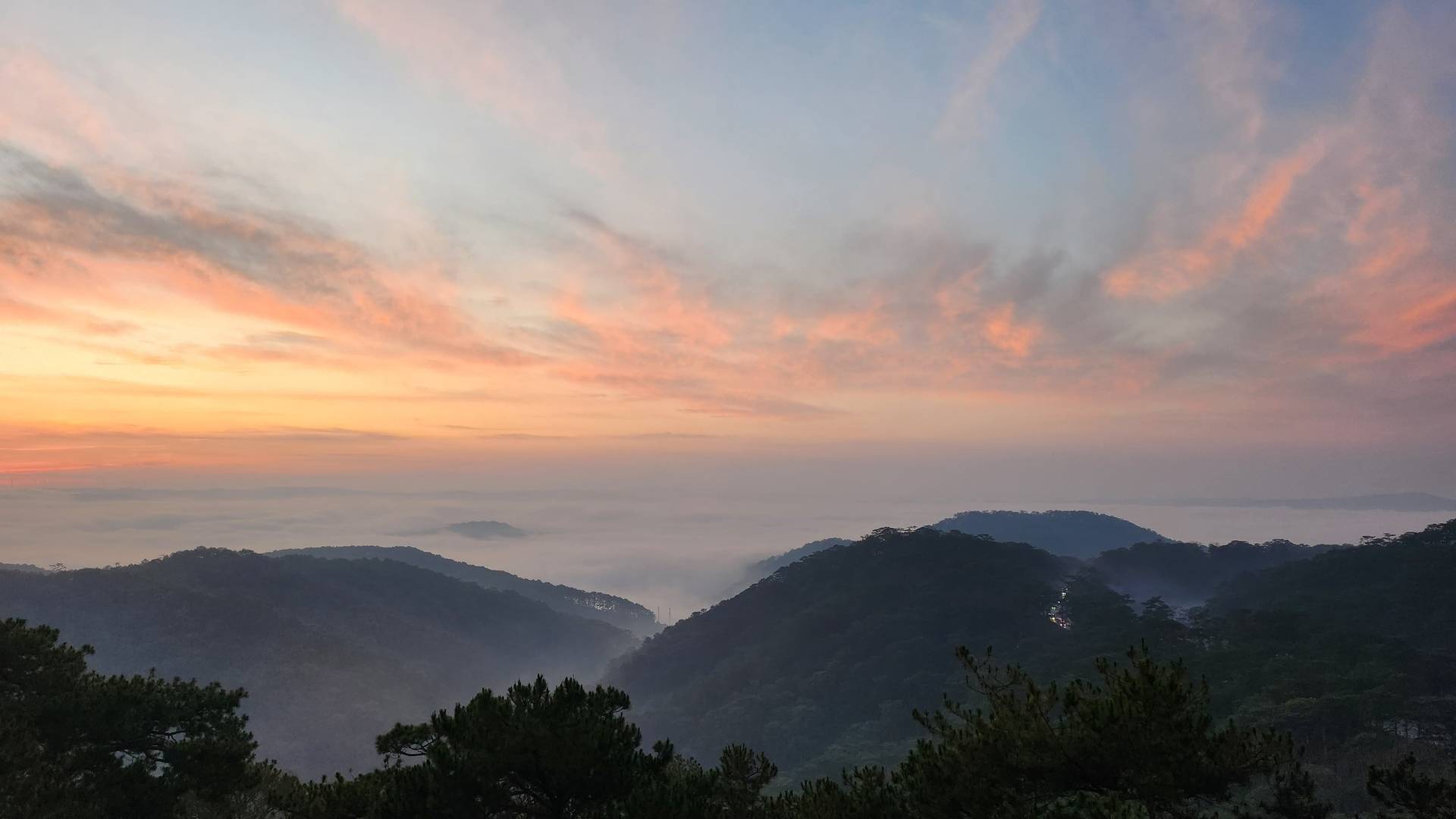 A serene mountain landscape blanketed in morning mist and layered peaks creates an ethereal sunrise scene over Đà Lạt's misty highlands.